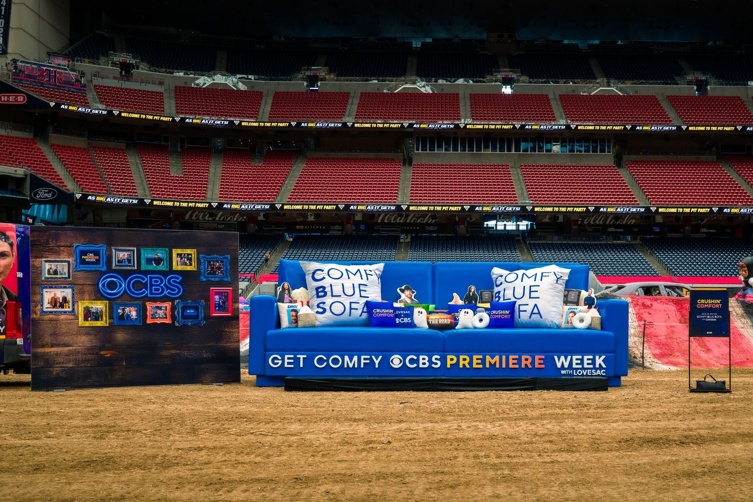 A panoramic view of an empty baseball stadium with red seats and advertising banners along the outfield walls.