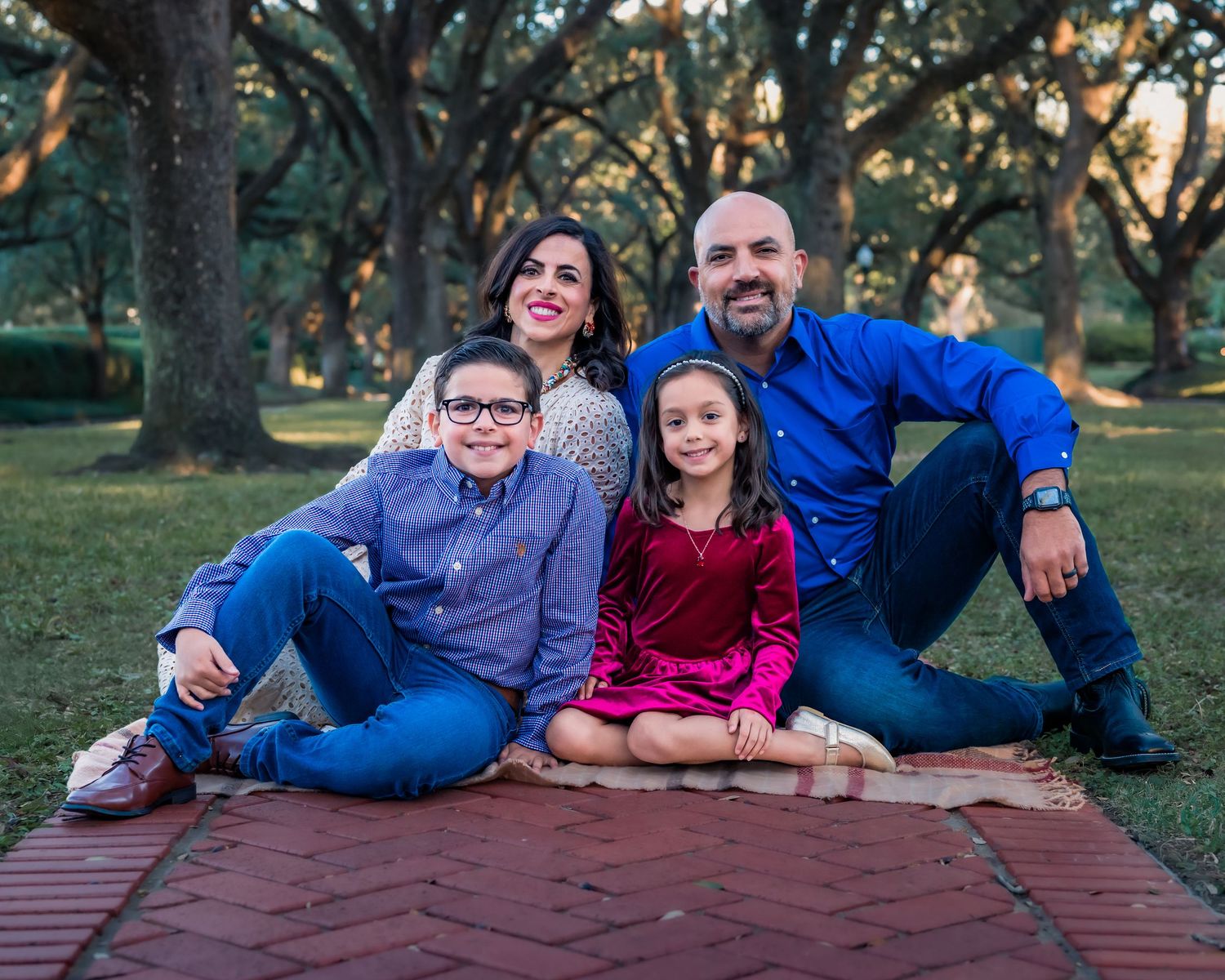 A family in coordinating blue and burgundy outfits poses together on a brown blanket outdoors during a photo session.