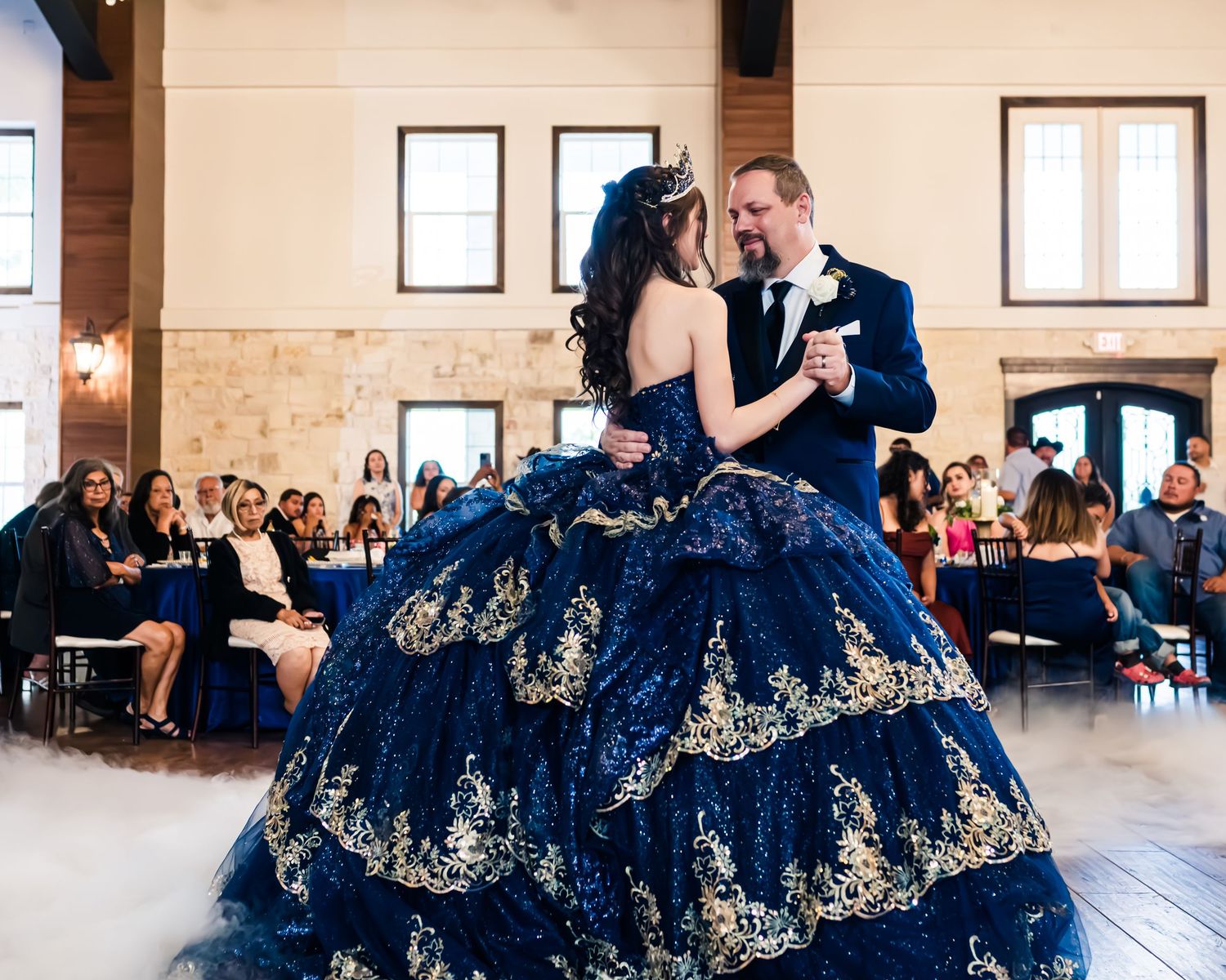 Couple dancing gracefully in a navy blue ballgown dress with gold embellishments at an elegant ballroom venue.