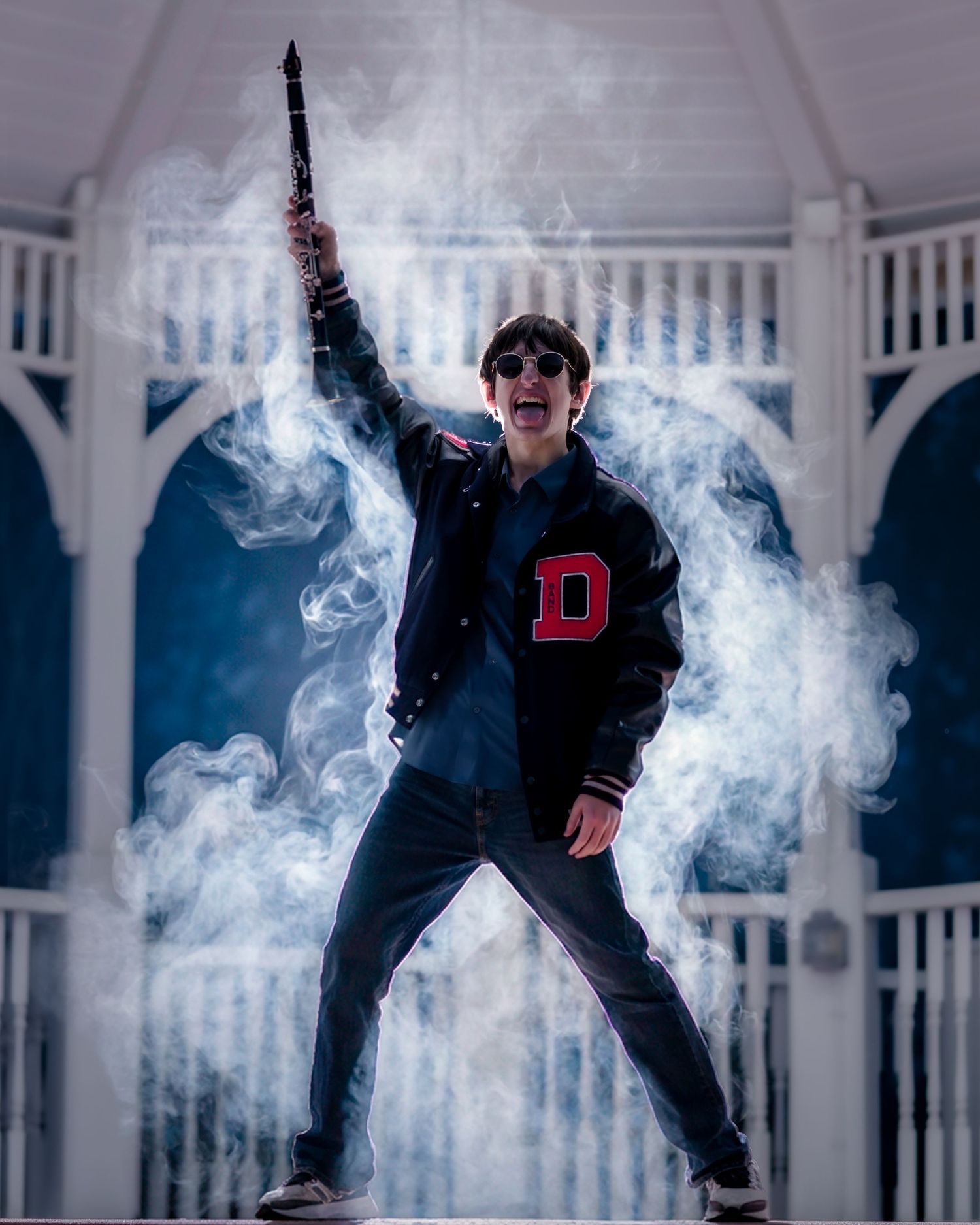 A person in a varsity jacket poses dramatically in front of a white gazebo surrounded by atmospheric smoke effects.