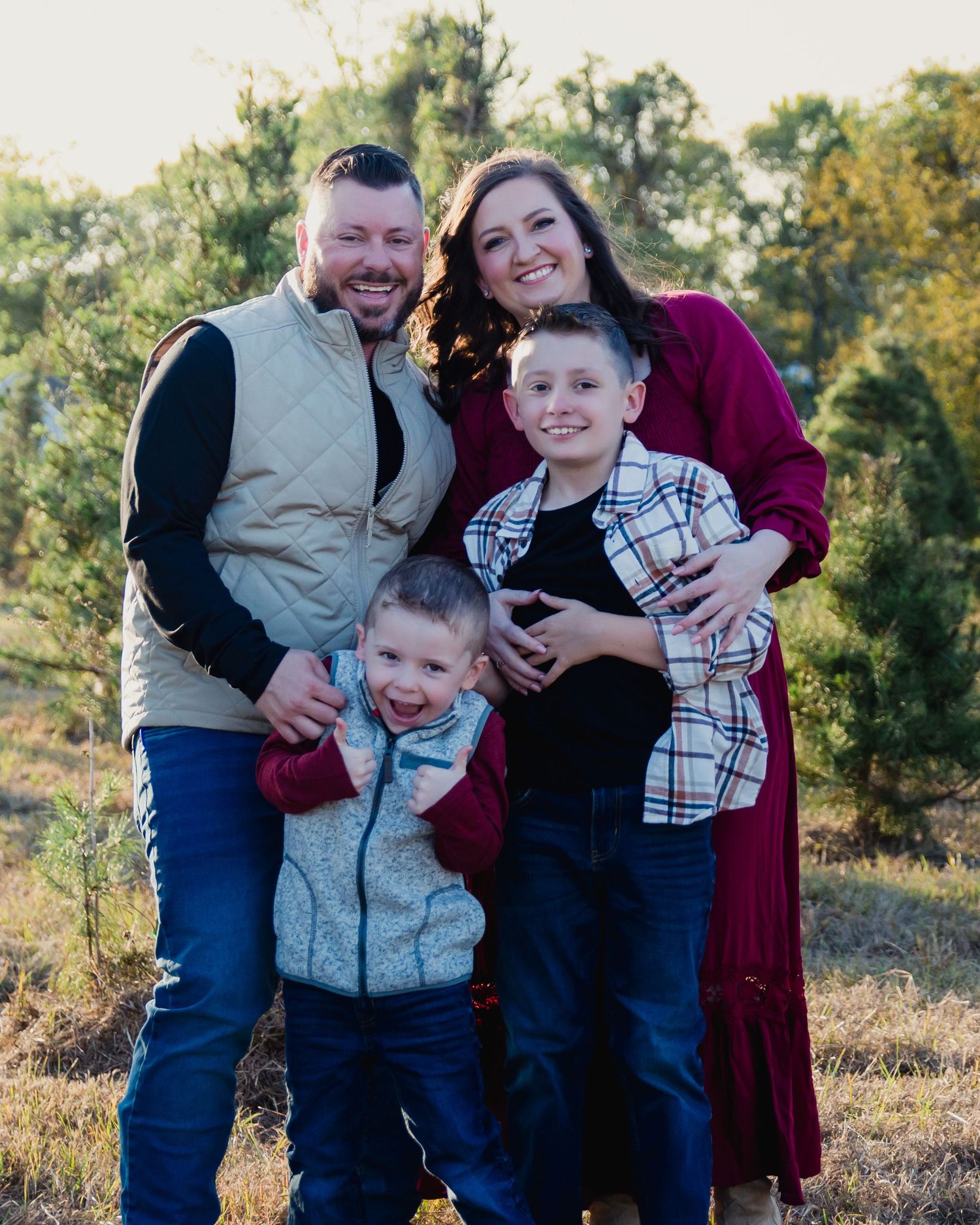 A family poses together outdoors in coordinated outfits with fall foliage in the background.