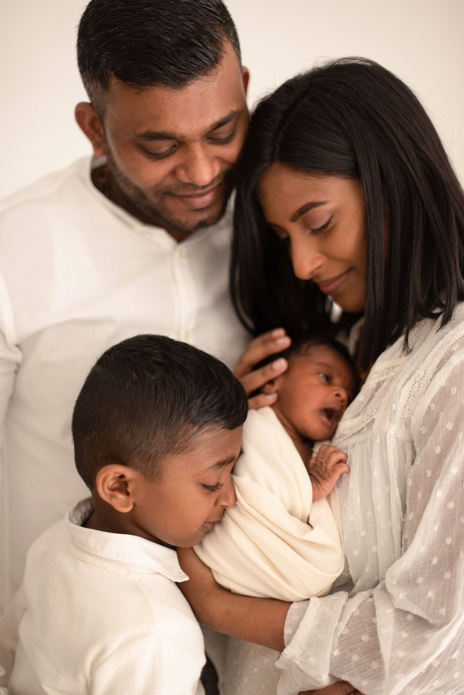 Family dressed in white shares an intimate moment with their newborn and young child.