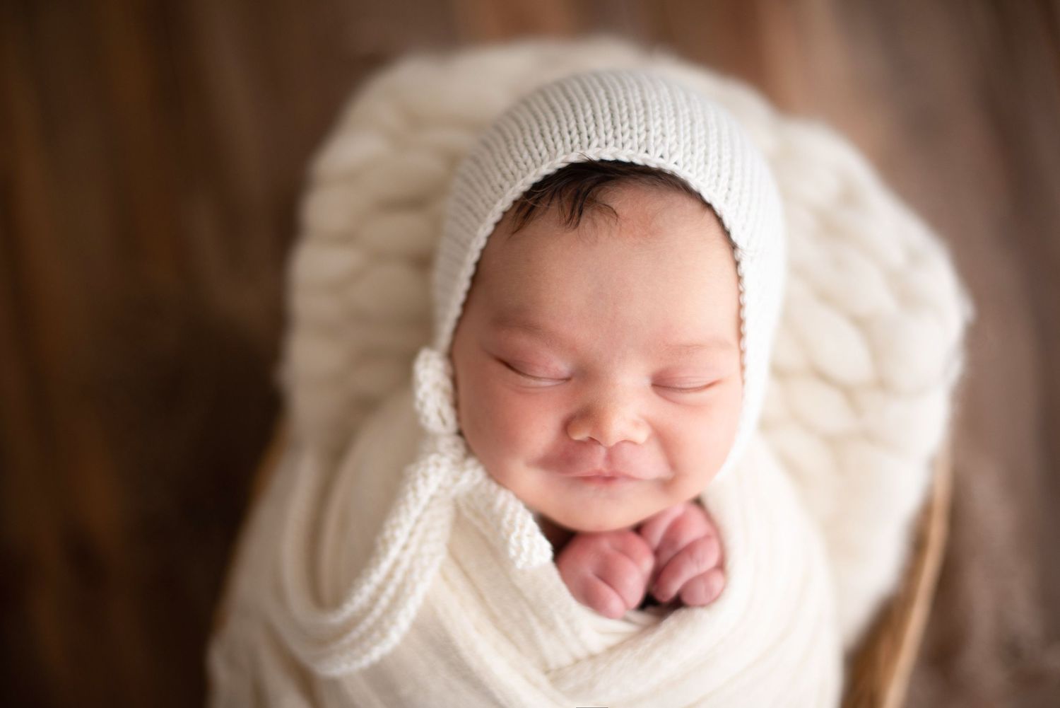 Newborn baby wrapped in cozy white knit wearing matching bonnet during photo session.