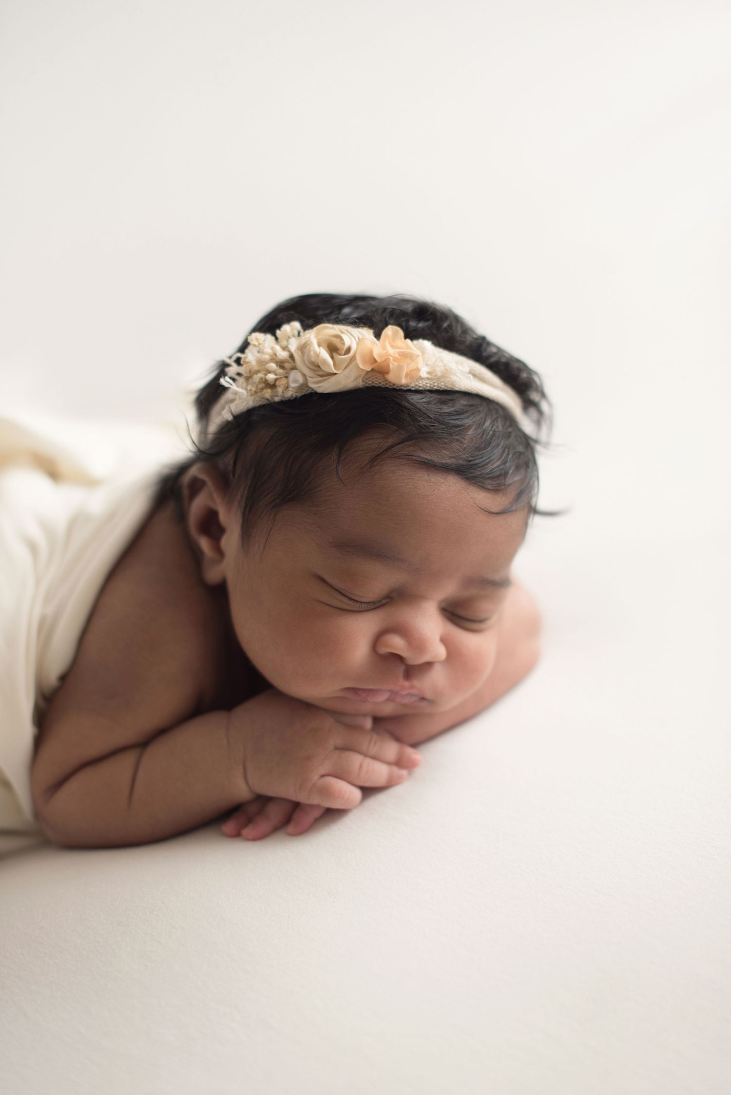Sleeping newborn wearing floral headband posed on white background.