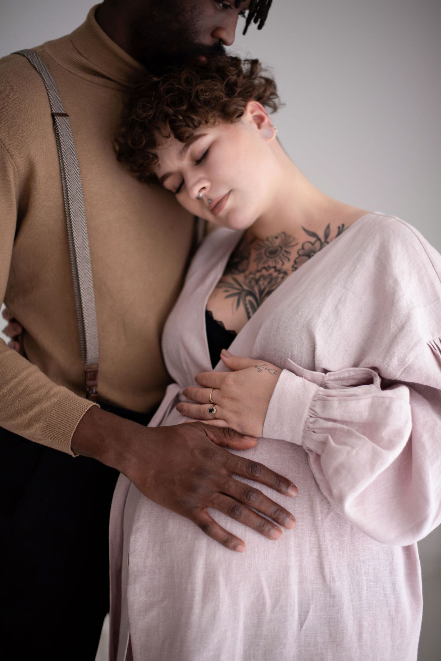 Couple in casual elegant wear shares tender moment during maternity photoshoot.