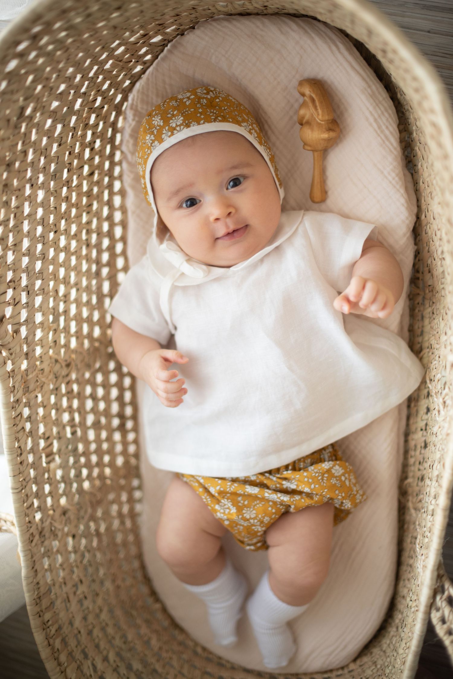 Infant in white top and yellow floral outfit resting peacefully in woven basket.