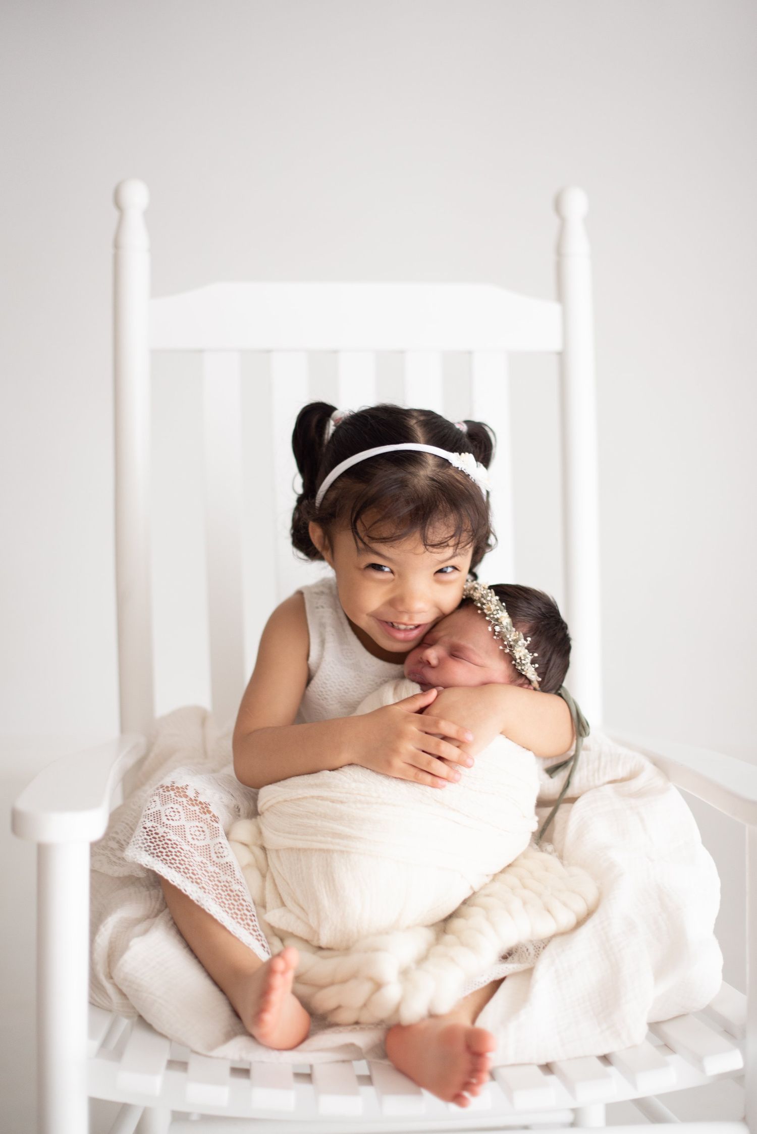 Tender sibling moment in white rocking chair during professional photo session.