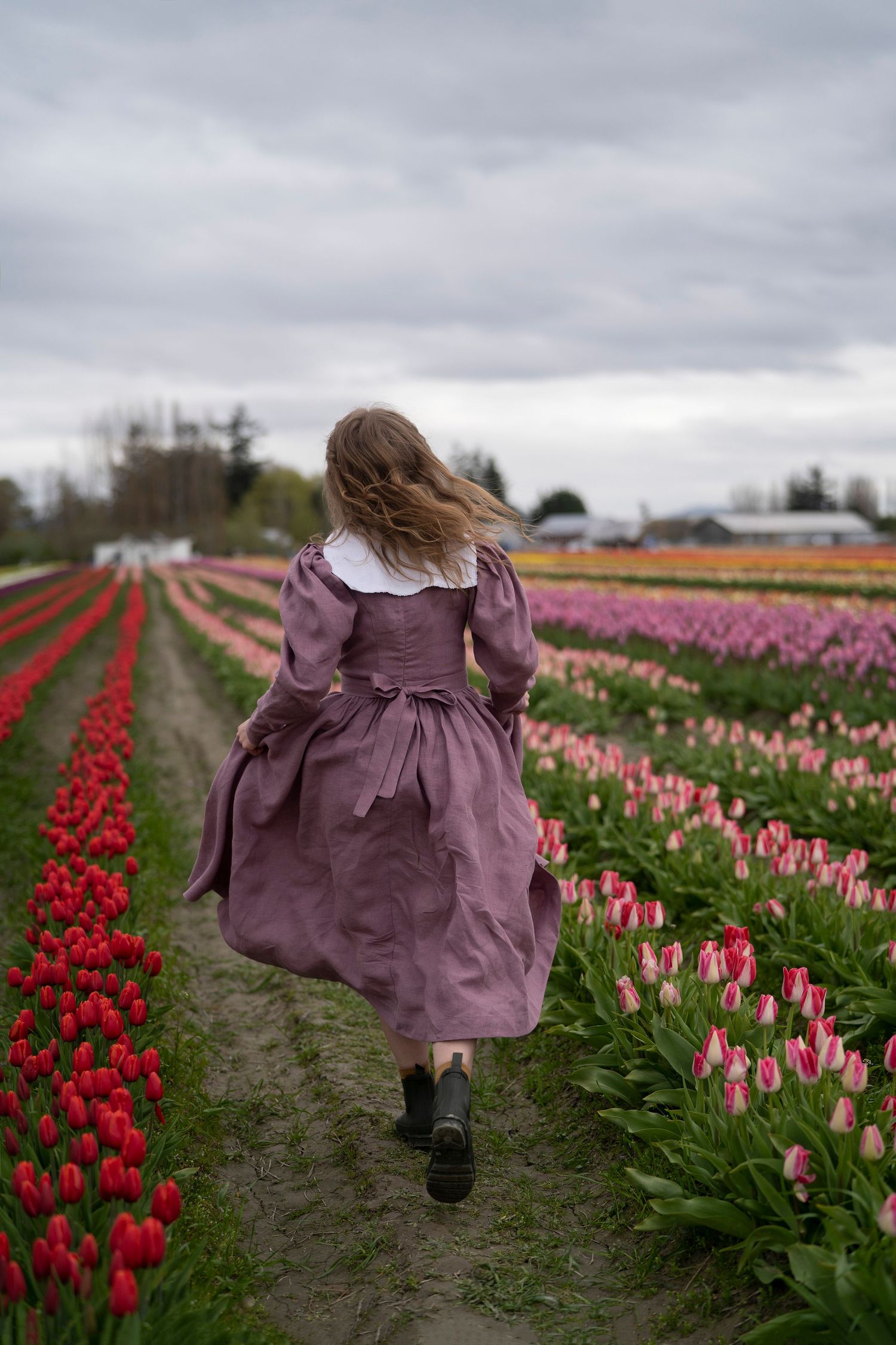Person in a purple vintage dress runs through rows of vibrant red and pink tulips on a moody spring day.
