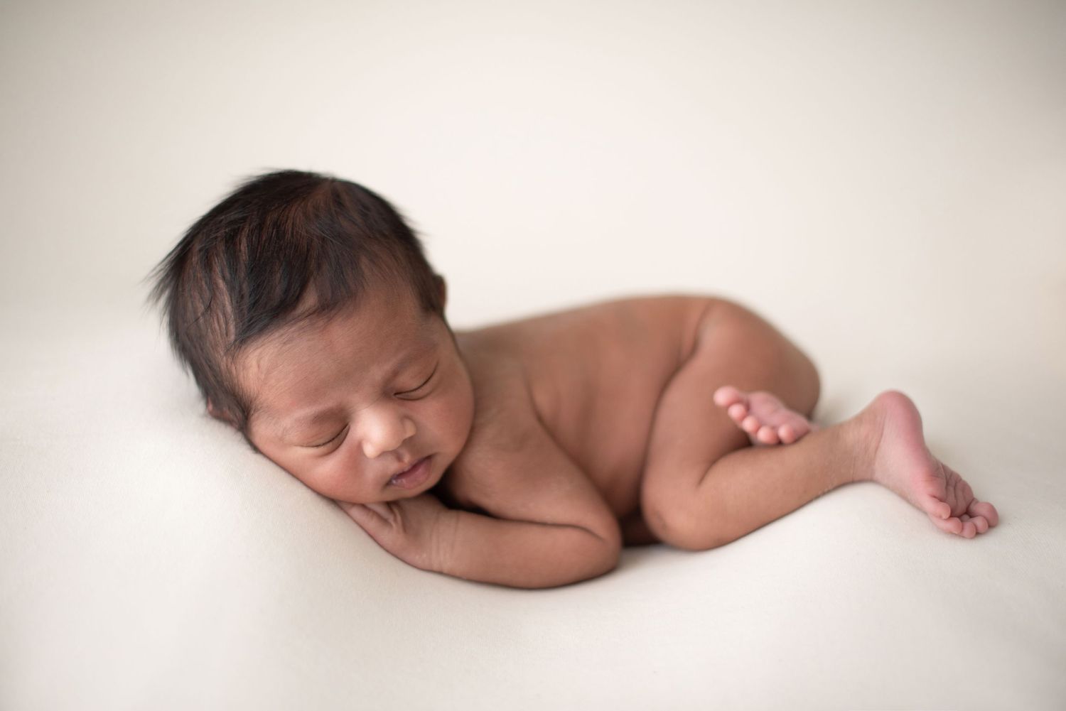 A serene newborn baby sleeps soundly in a natural pose on white fabric.