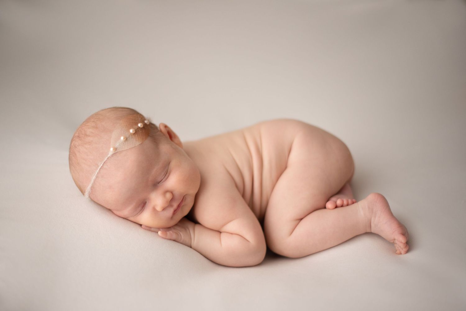 Sleeping newborn in fetal position with delicate headpiece during professional photo session.