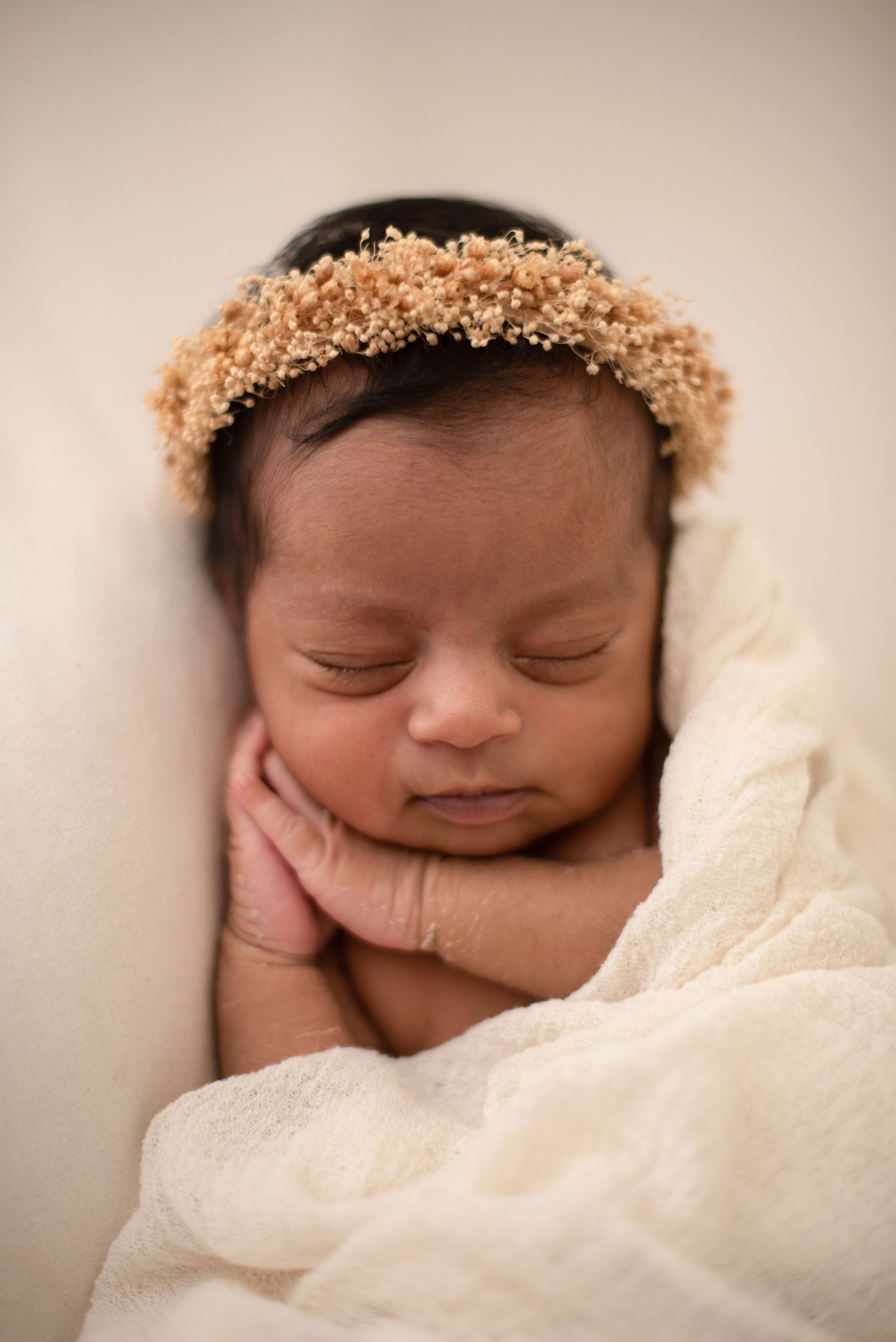 A sleeping newborn baby wearing a delicate golden crown rests peacefully on white fabric.