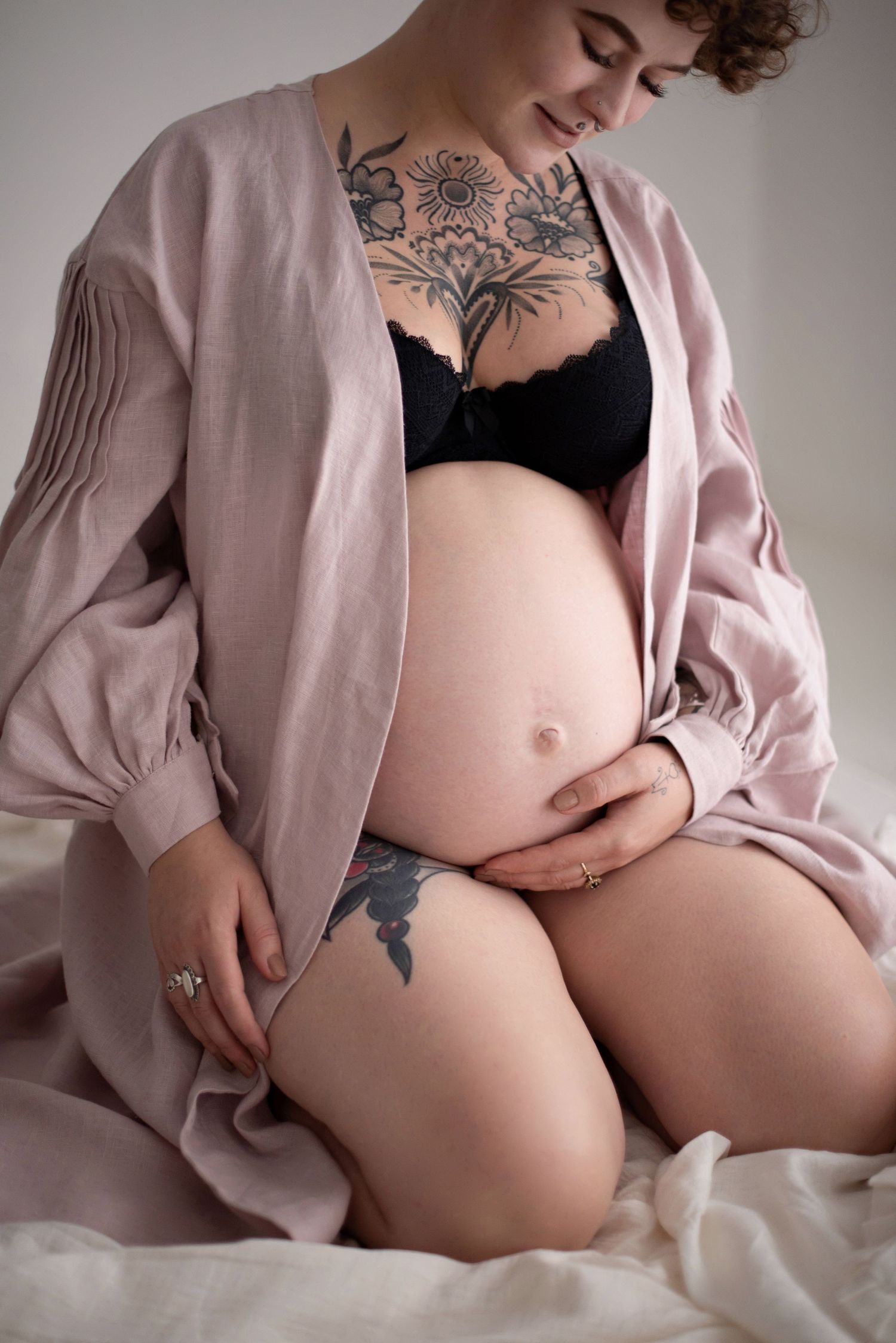 Close-up maternity portrait highlighting tattoos and baby bump with pink robe and black lingerie.