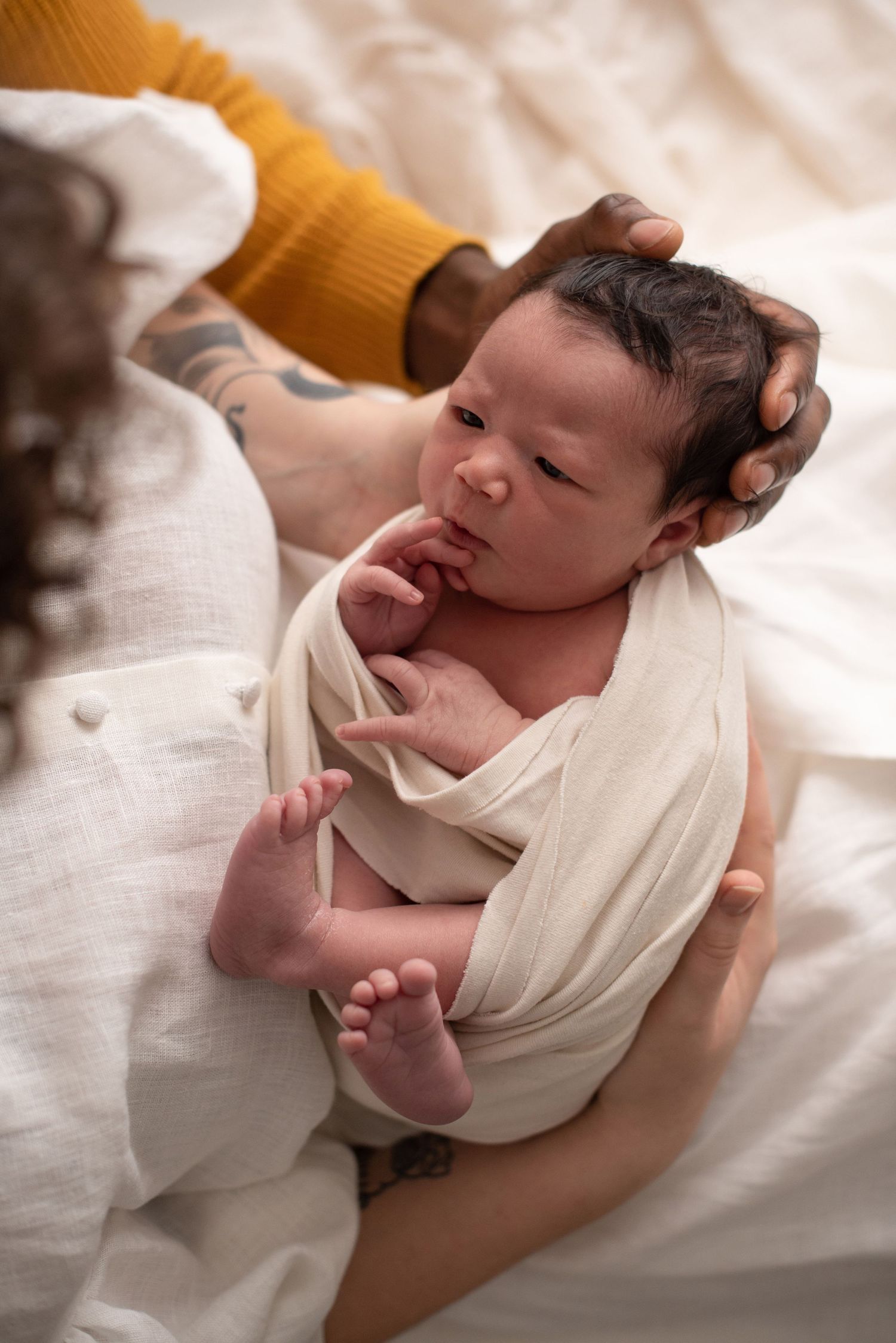 A close-up of a newborn baby partially wrapped in white fabric with tiny feet visible.