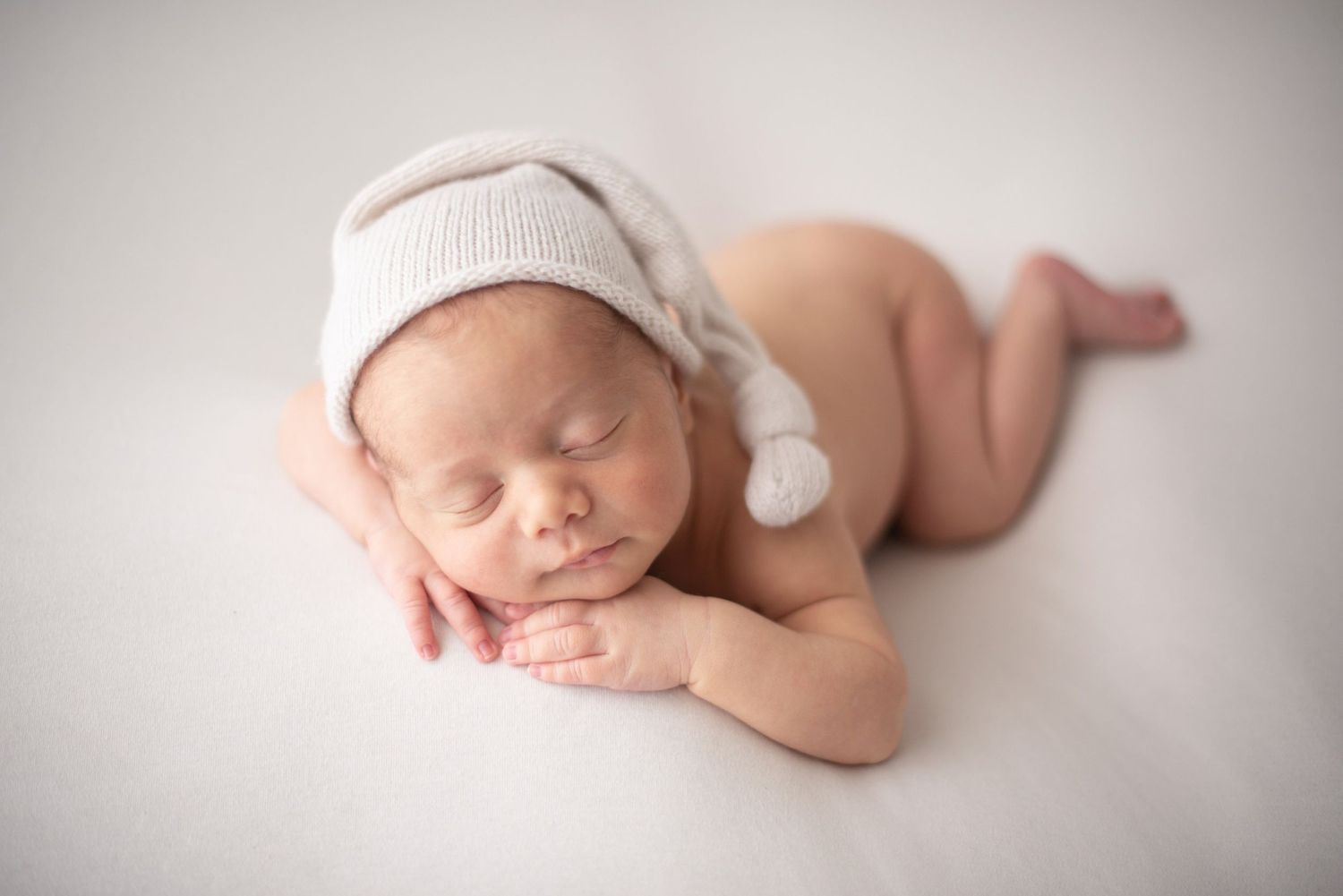 Sleeping newborn wearing white knit hat during professional photo session.