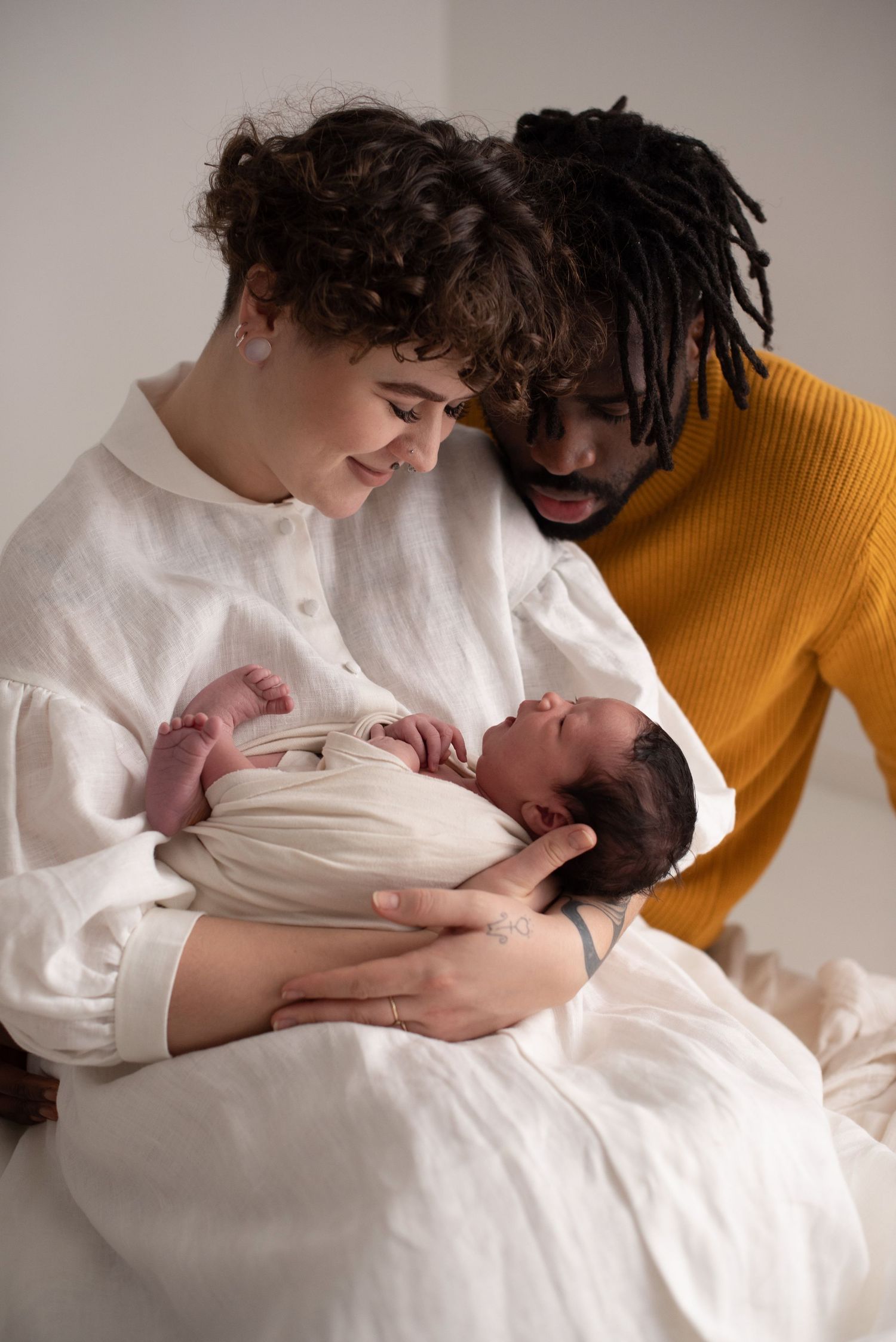 Parents share a tender moment looking down at their newborn during a professional photo session.