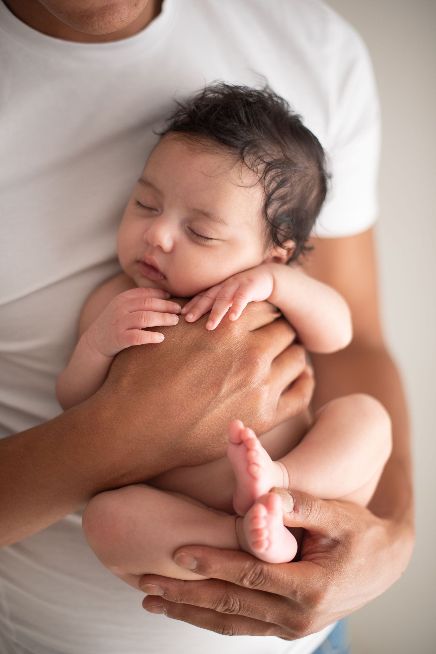 Sleeping newborn baby resting peacefully on parent's hands against white background.