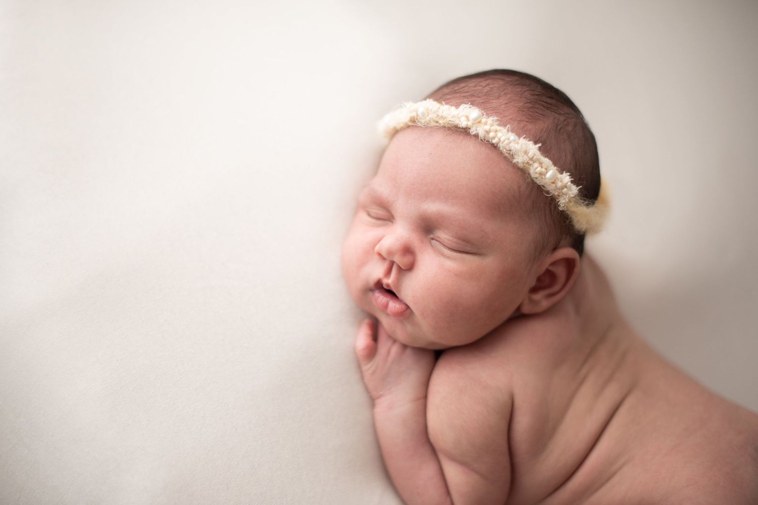 Peaceful sleeping newborn with pearl headband against soft white background.