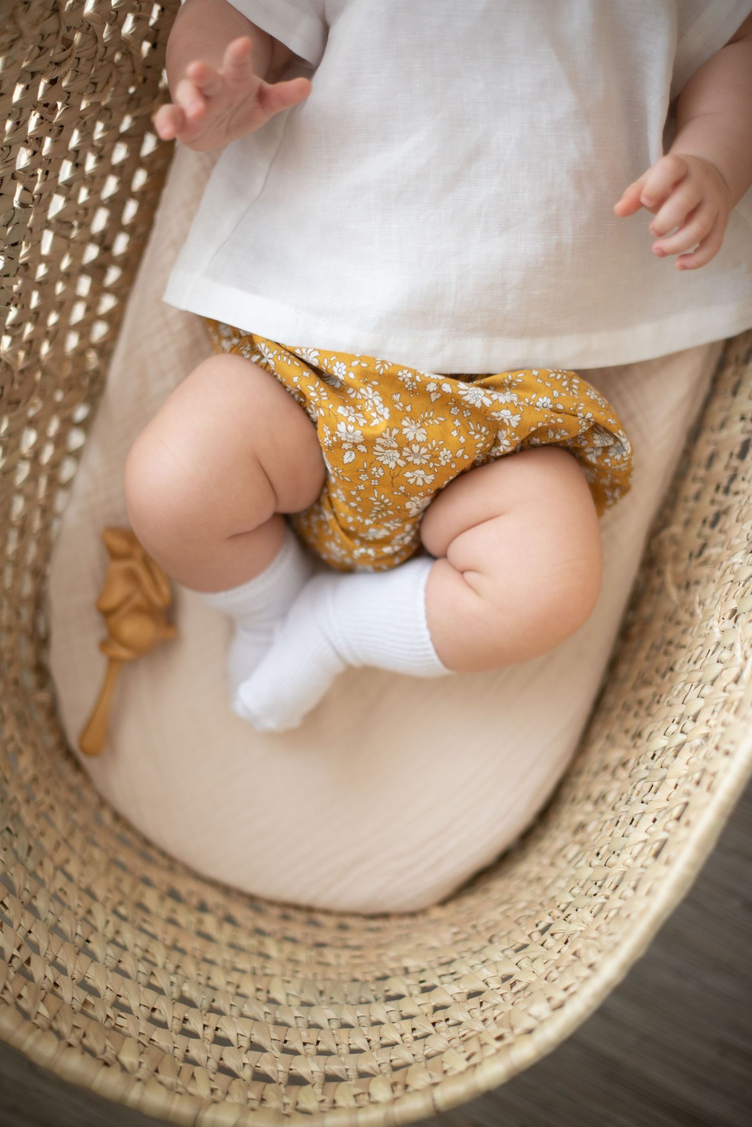 Close-up of baby legs in yellow floral bloomers resting in woven basket.