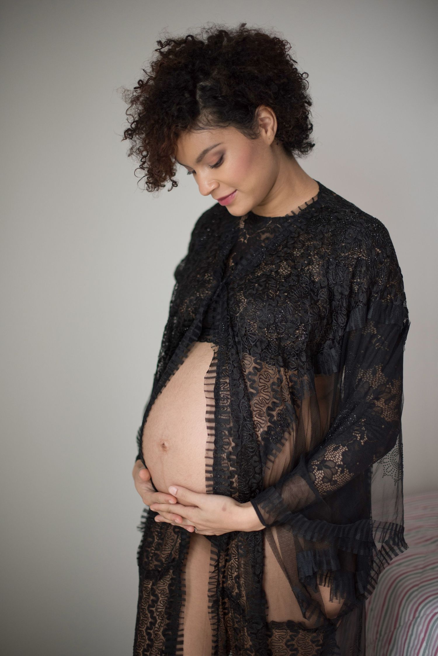 Expecting mother in black lace robe cradles her belly during a maternity photoshoot.