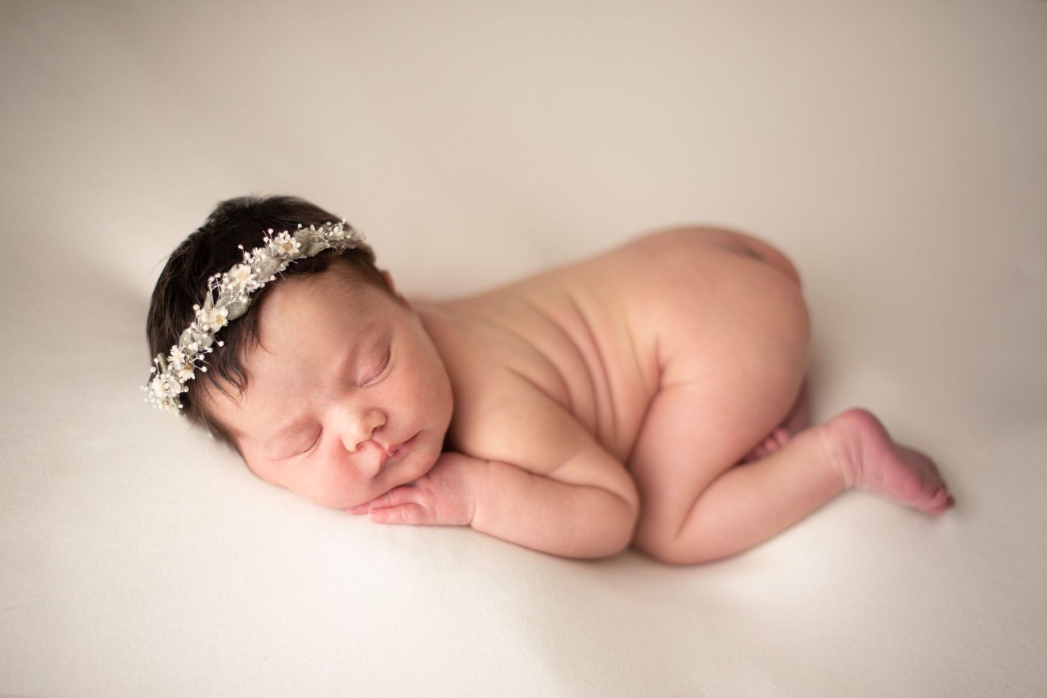 Peaceful sleeping newborn with crystal headpiece posed on soft cream background.