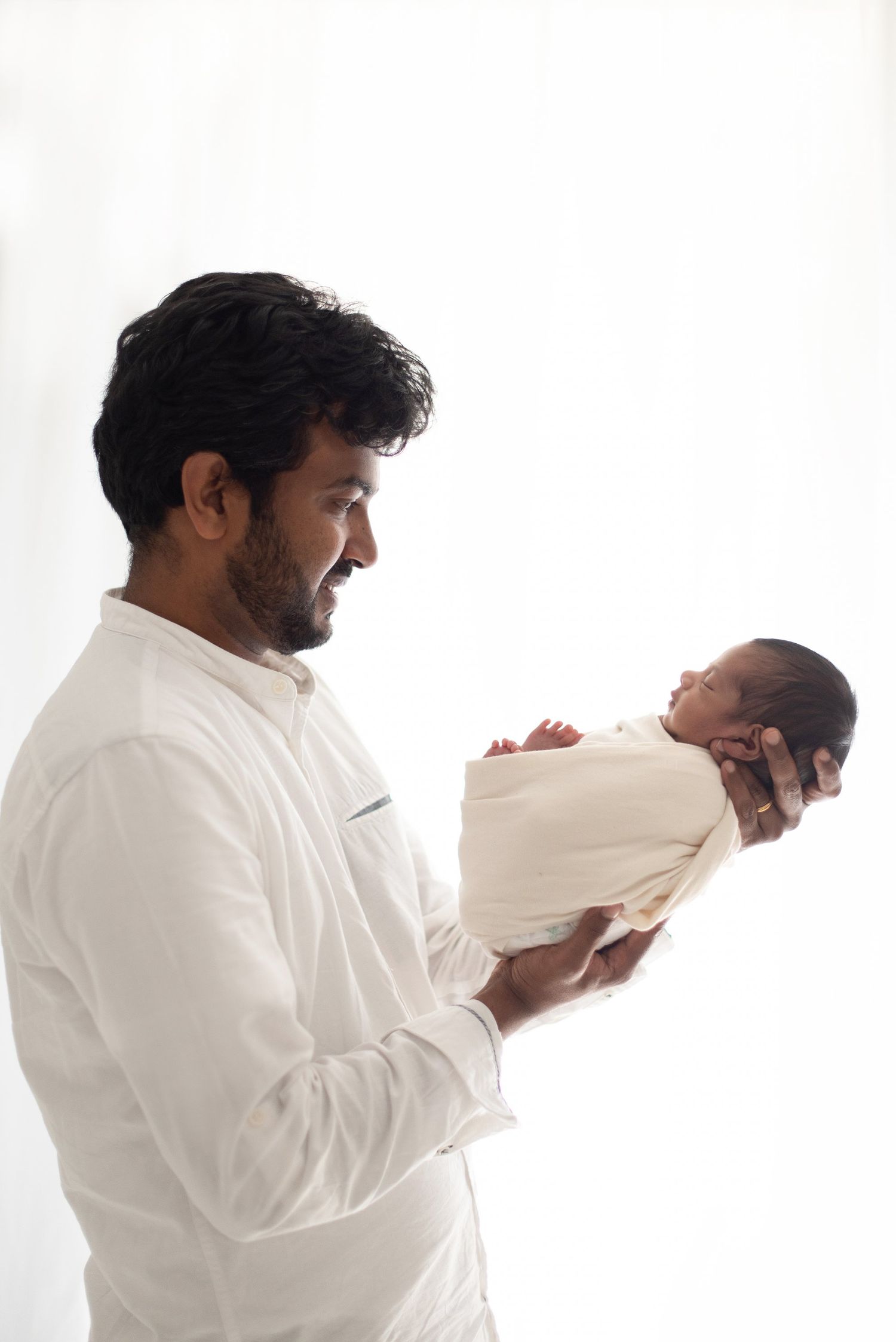A tender moment as a parent in white clothing gently holds their newborn baby wrapped in cream-colored fabric.