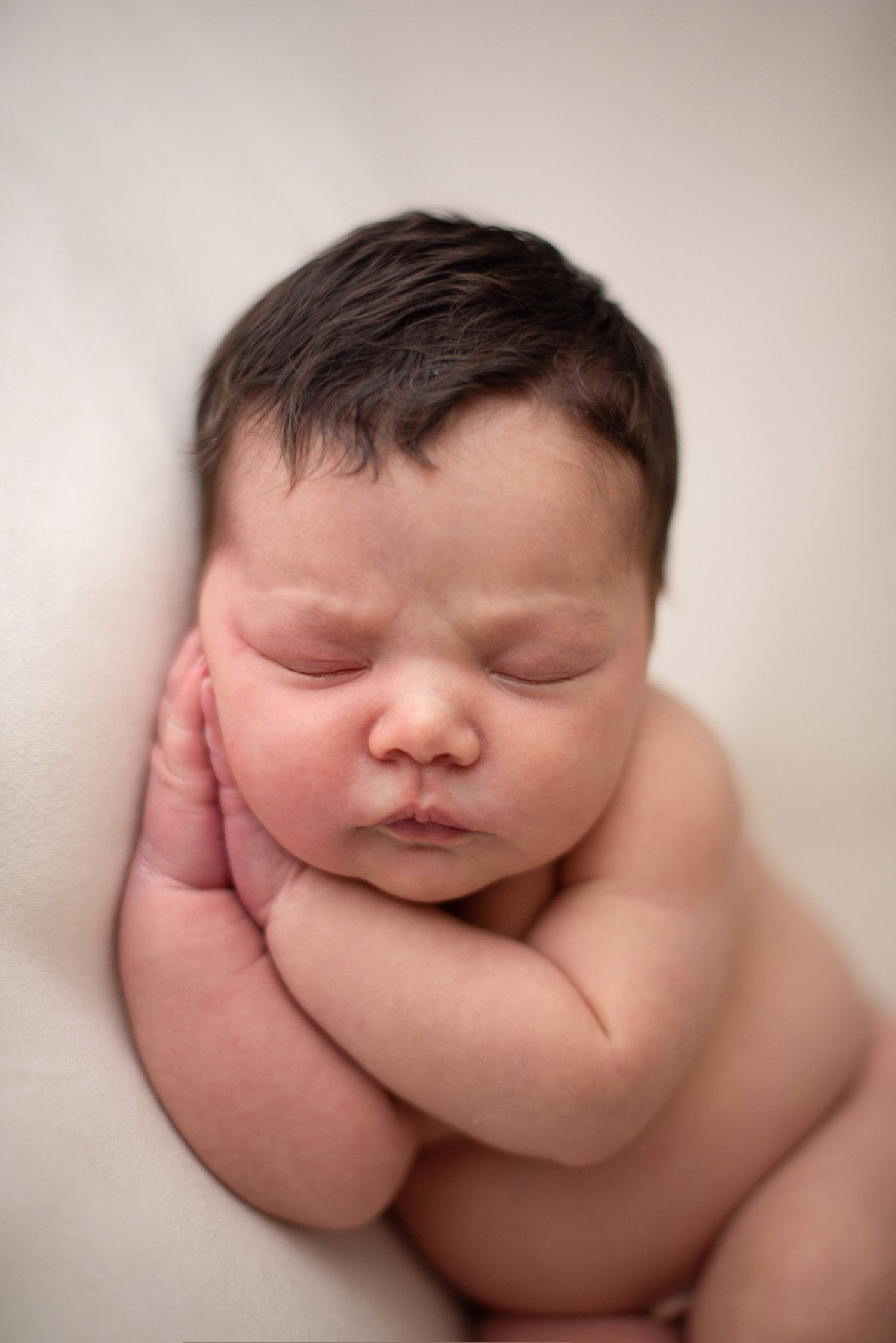 Close-up of peaceful sleeping newborn with hand resting near face.