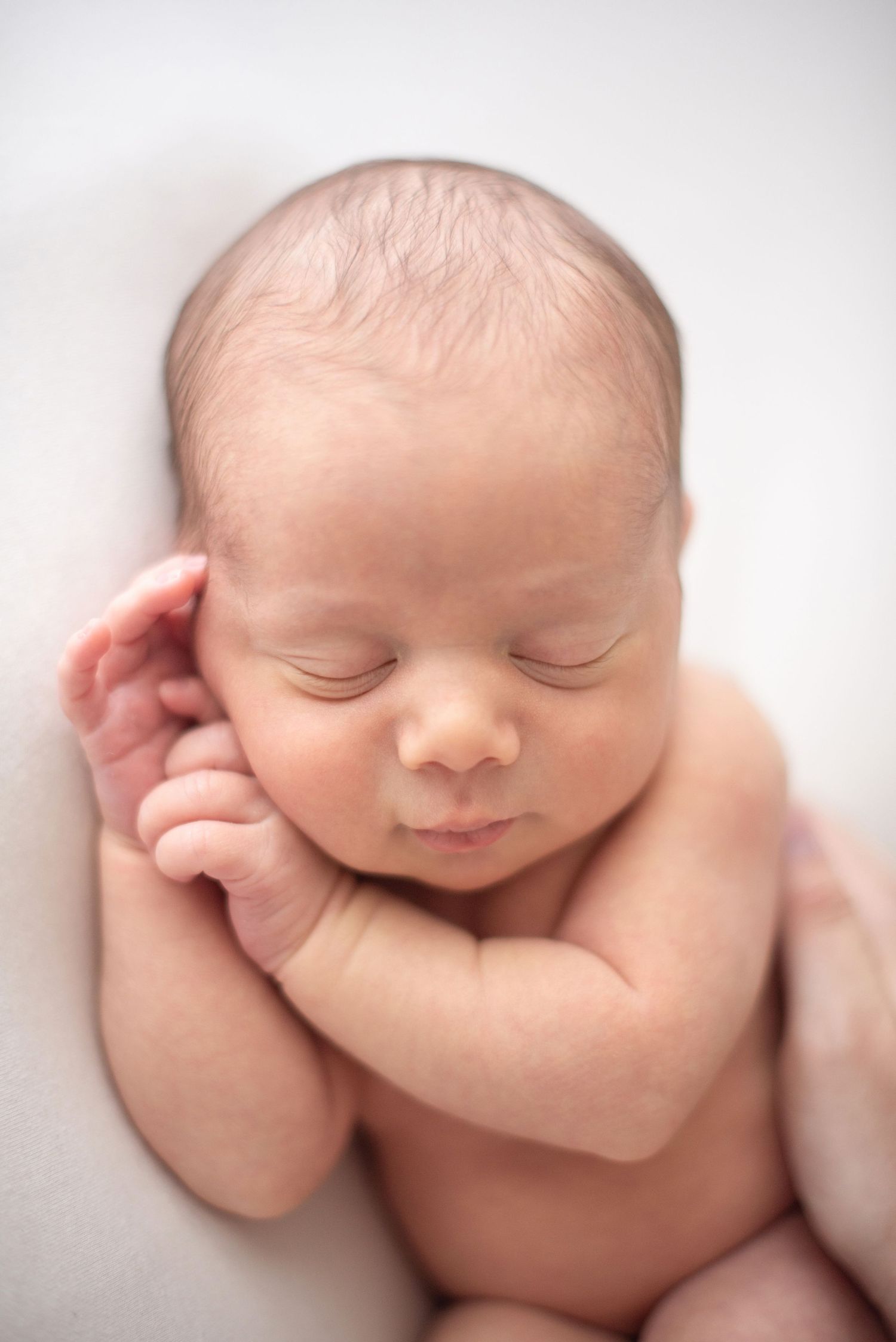 Sleeping newborn baby with delicate features resting on a soft white surface.