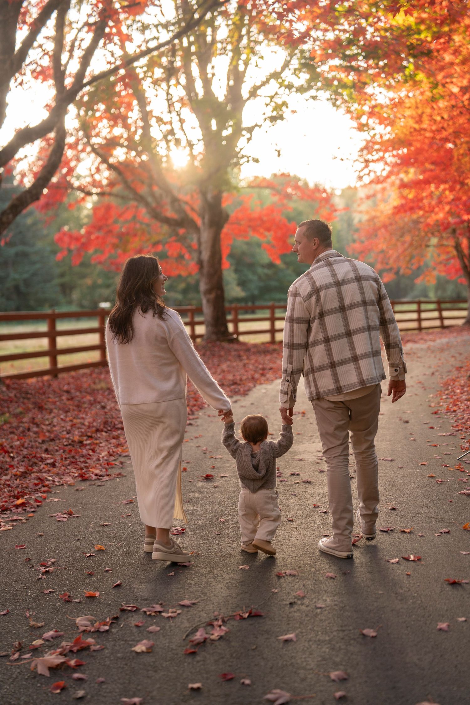 A family walks hand in hand down a path surrounded by vibrant red autumn foliage during golden hour.