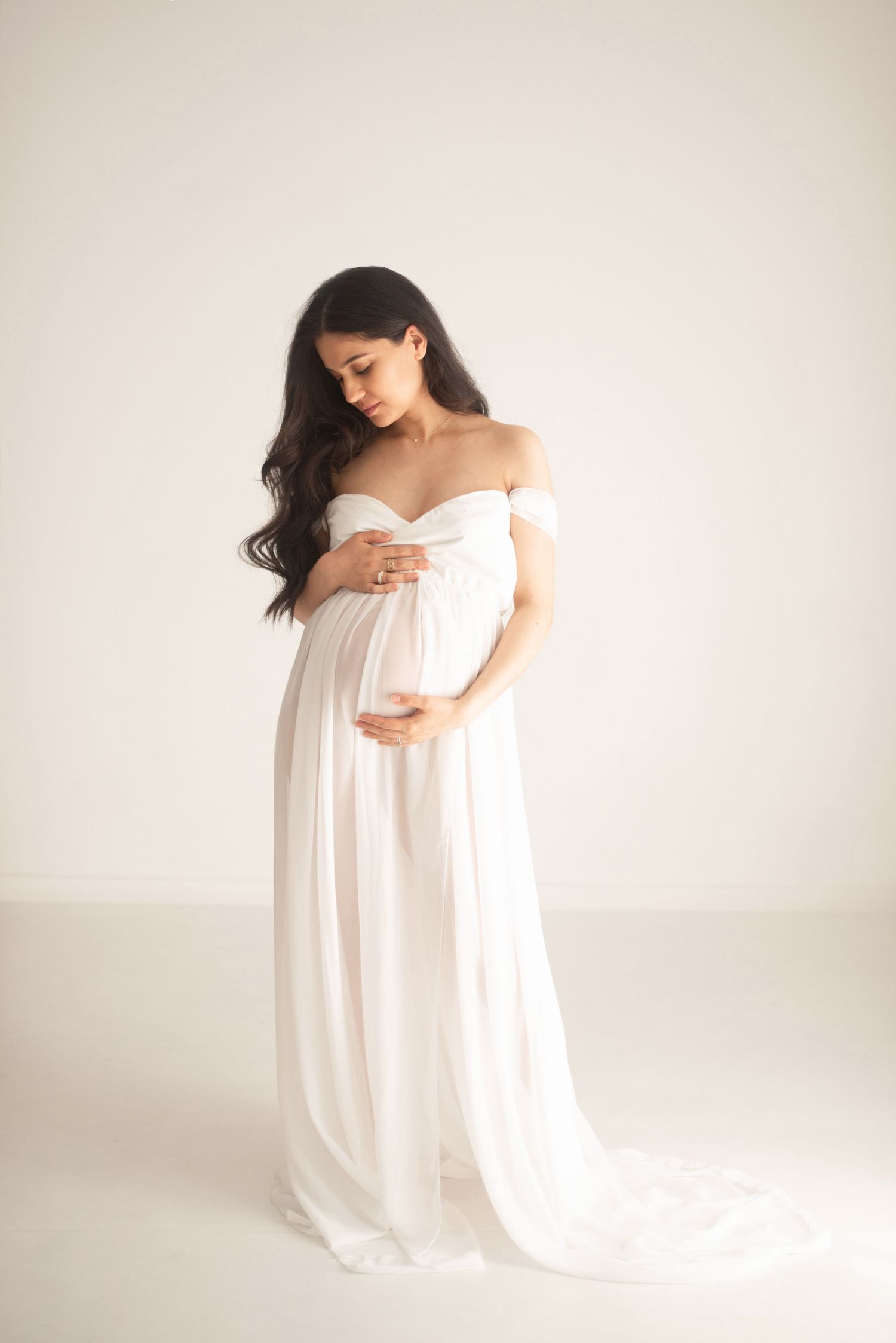 Ethereal maternity portrait in flowing off-shoulder white gown with train.