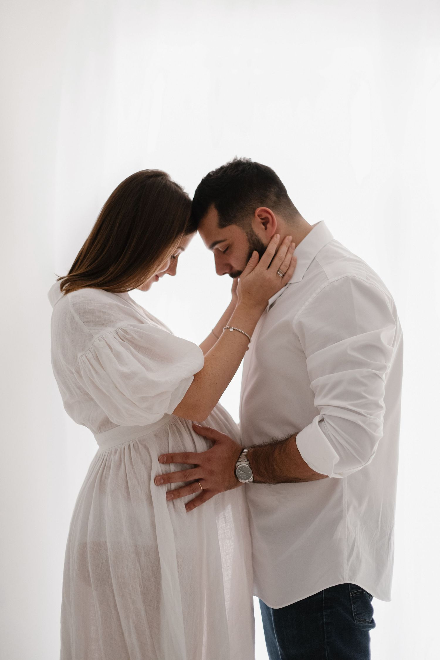 A tender moment between a couple in white clothing against a light background.
