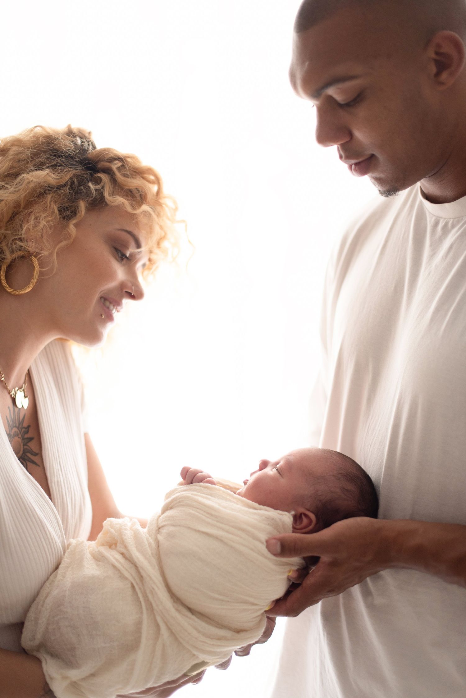 Intimate family portrait of new parents tenderly holding their swaddled newborn baby.