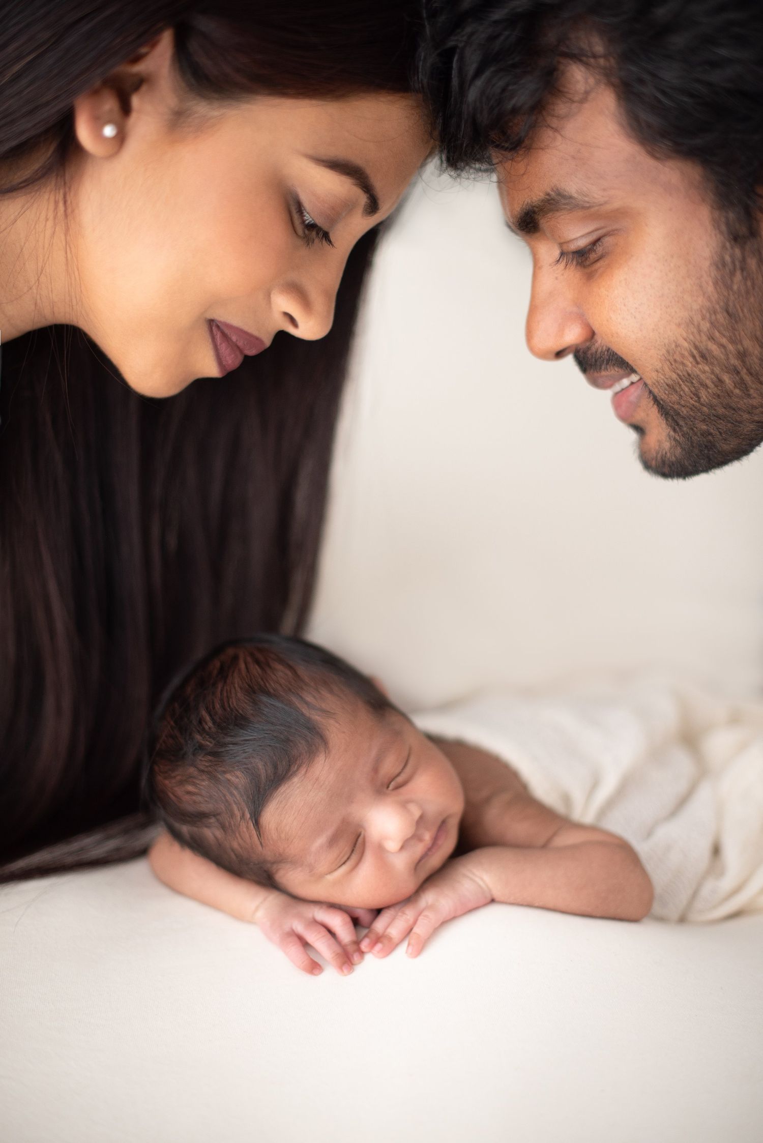 A tender moment with parents gazing lovingly at their sleeping newborn baby against a white background.