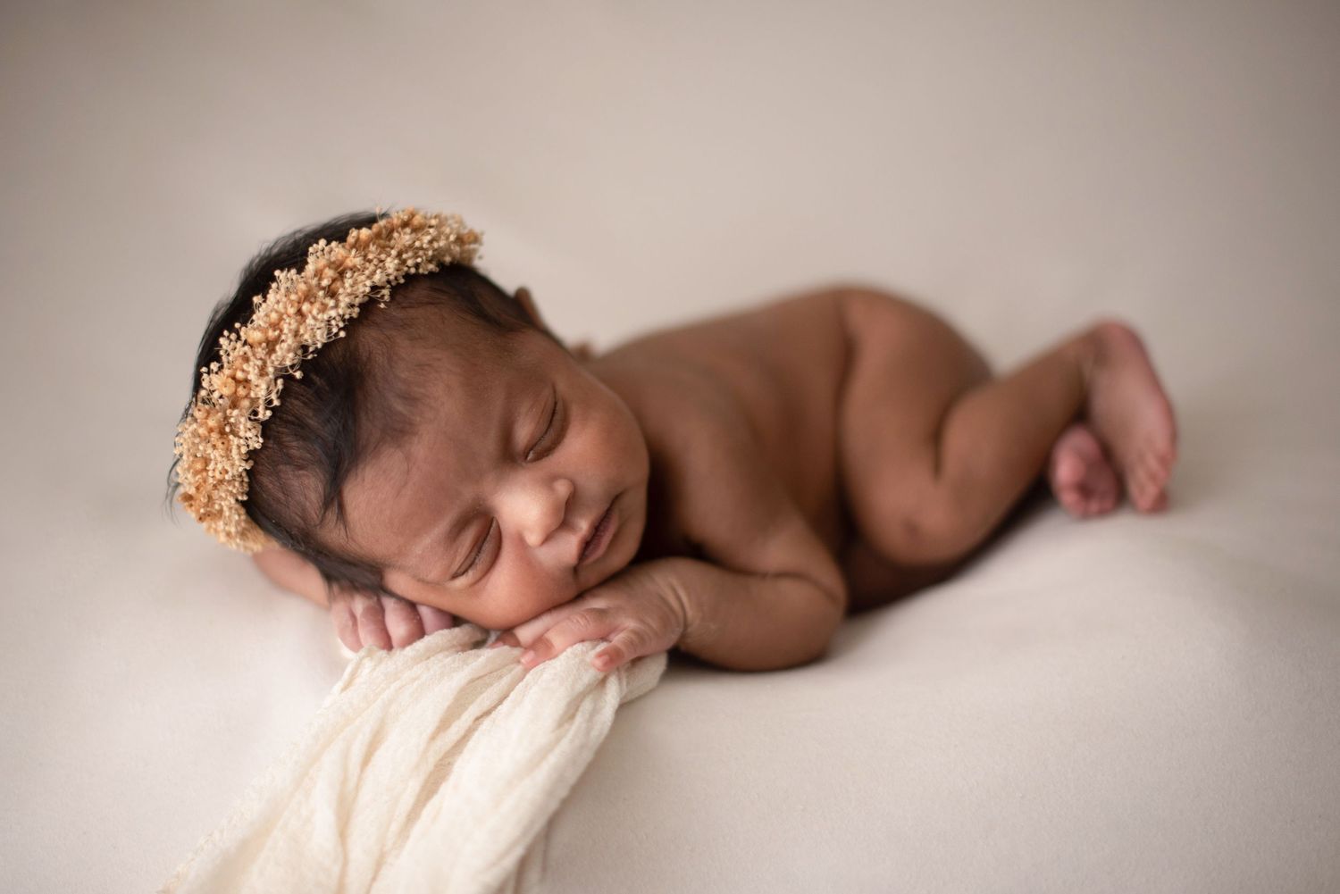 A sleeping newborn baby wearing a golden crown poses during an artistic photography session.