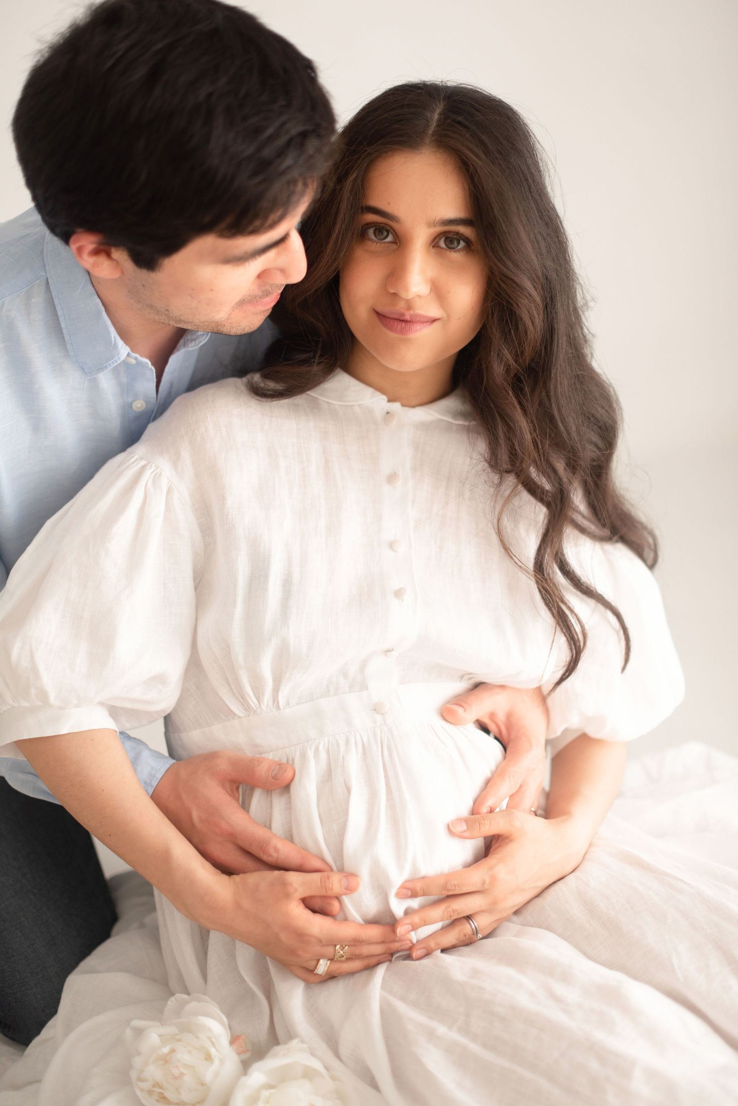 Intimate maternity portrait of couple in light clothing sharing tender moment.