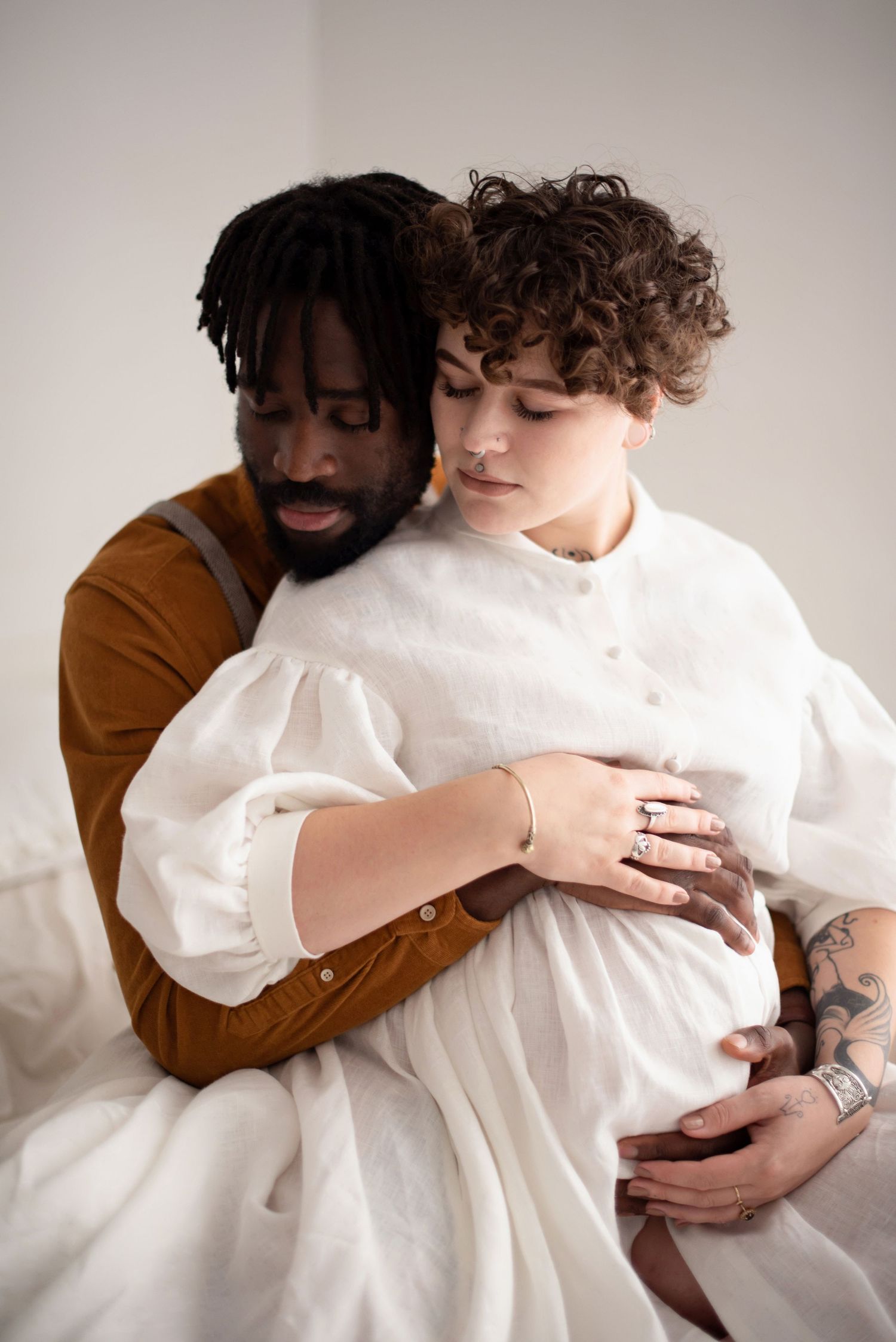 Intimate maternity portrait showing gentle embrace against light background.