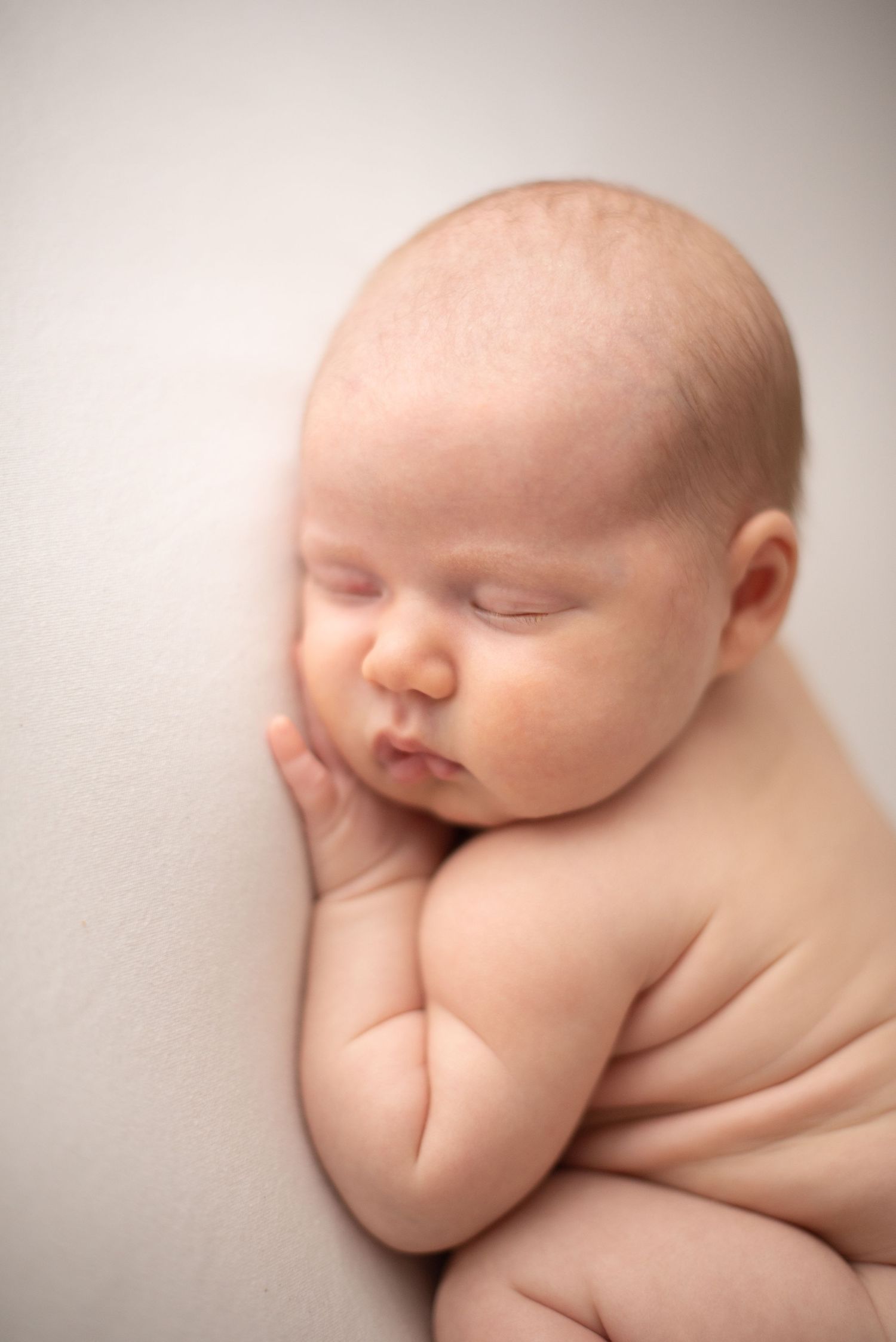 Sleeping newborn with hand under cheek posed on soft beige backdrop during studio photography.
