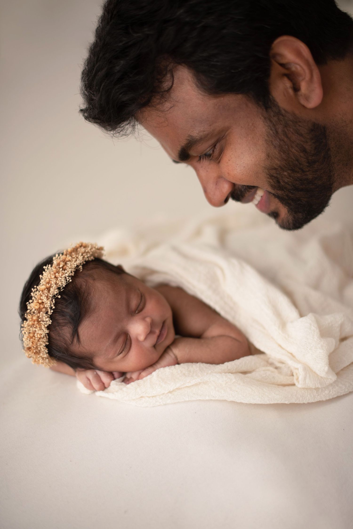 A peaceful portrait of a newborn baby wearing a delicate gold crown headpiece sleeping on white fabric.