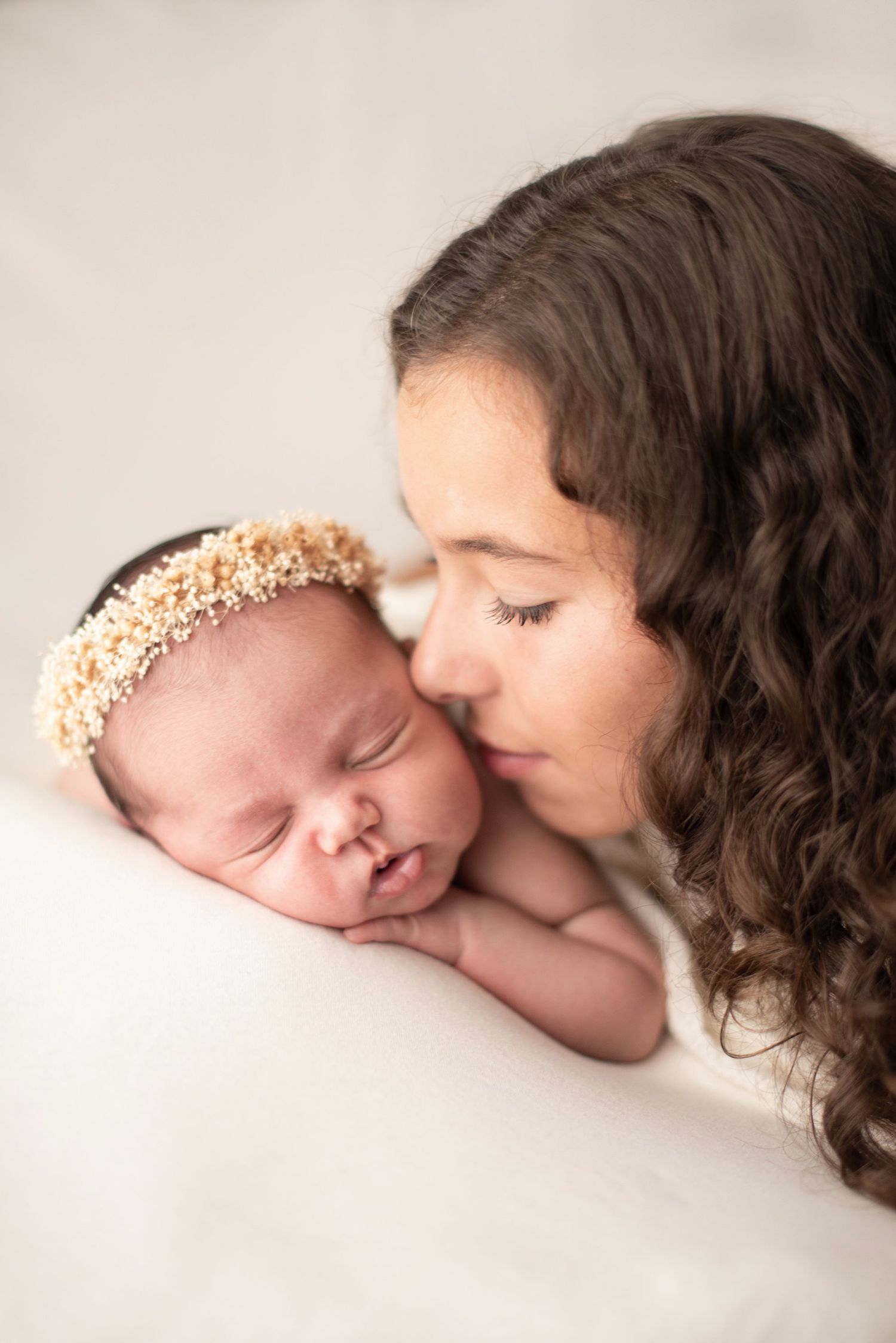 A tender moment of intimacy between parent and sleeping newborn wearing a delicate pearl headband.