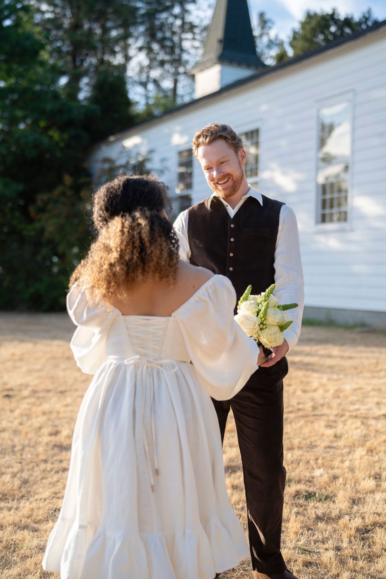 A romantic wedding photoshoot in a field with a white church in the background at golden hour.
