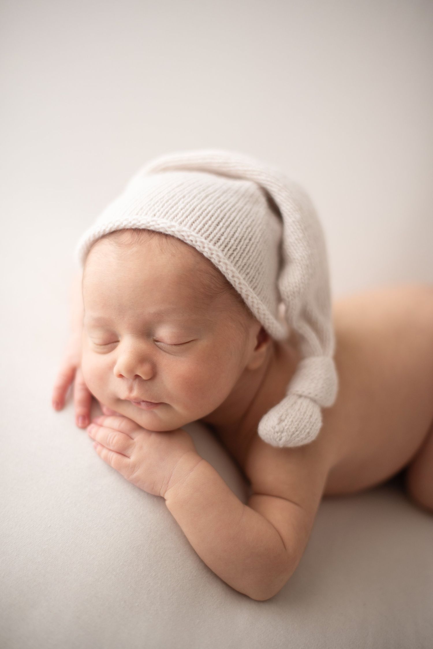 Peaceful newborn in soft white hat resting on cream backdrop.