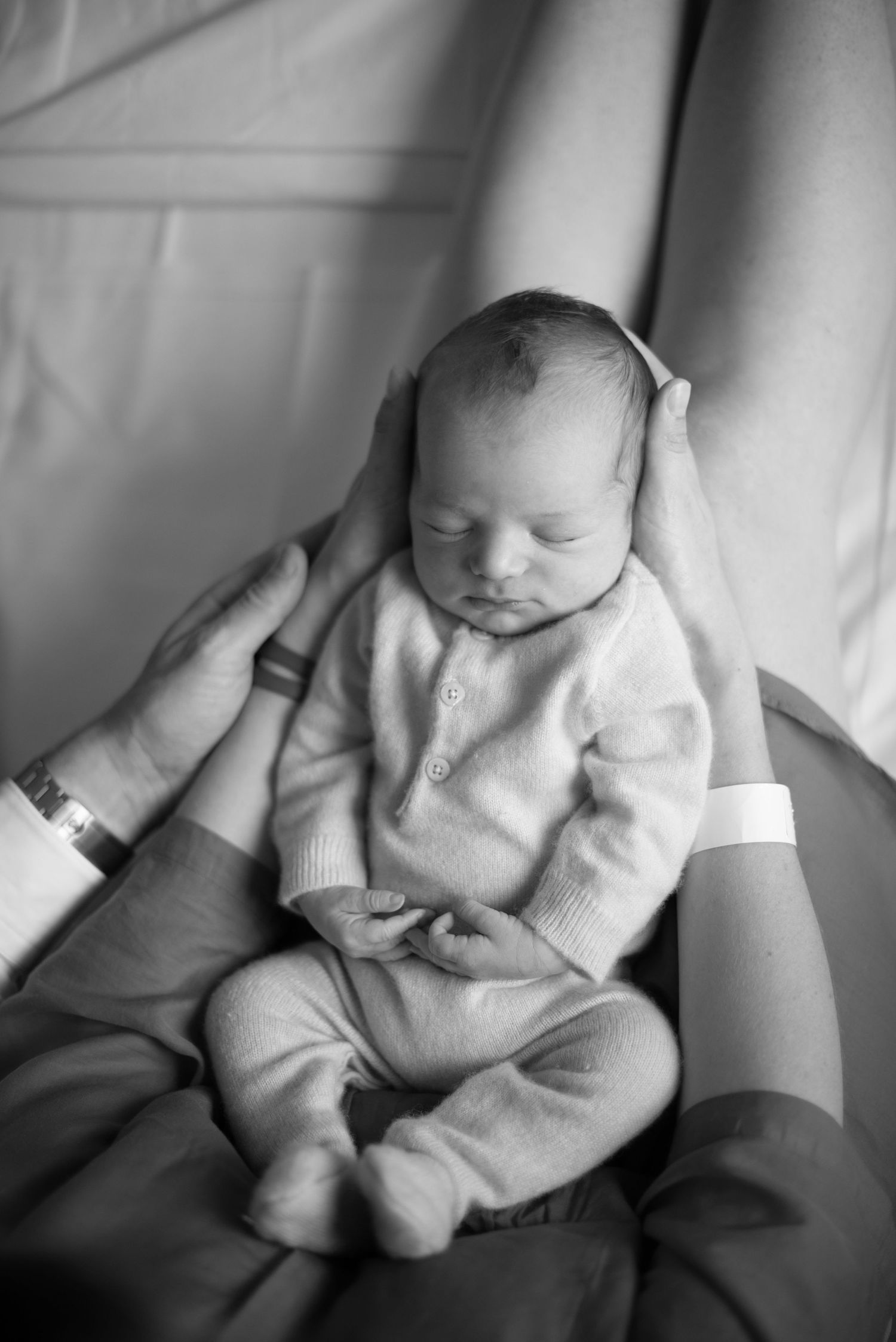 A peaceful newborn baby sleeping in a cozy white sweater while resting on someone's lap, captured in black and white.