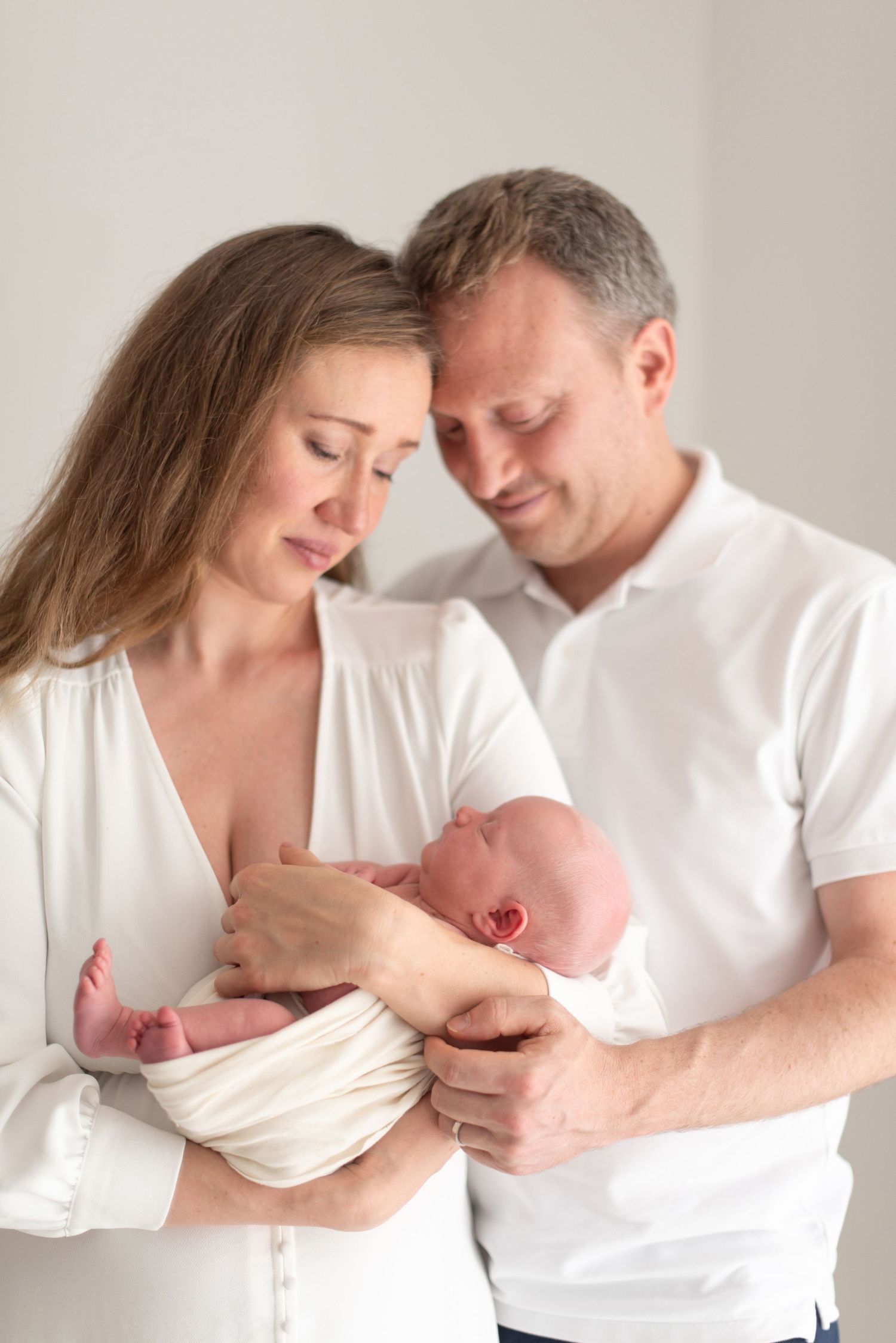 Intimate moment of new parents in white clothing cradling their newborn baby.