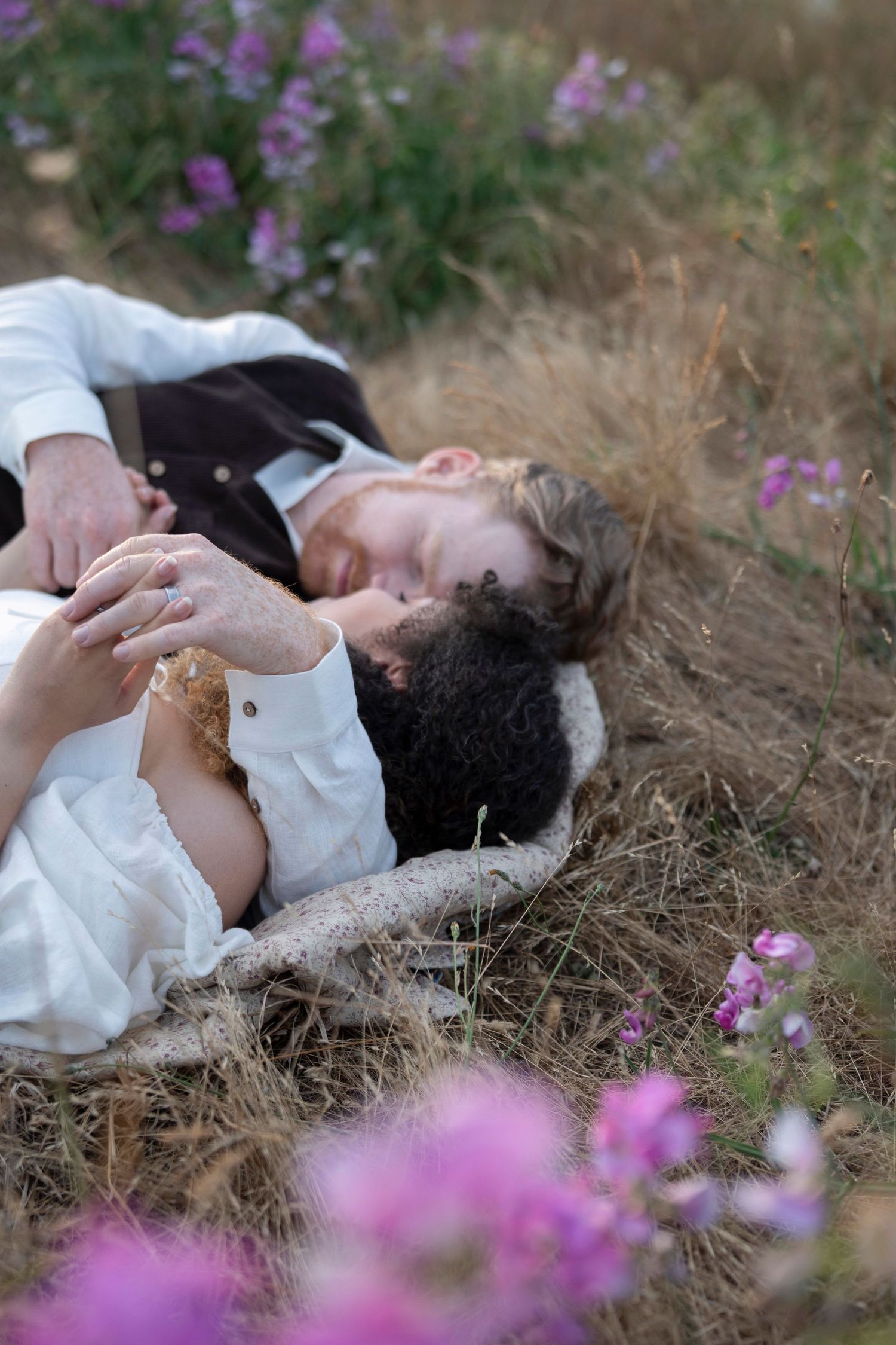 A person in white lies peacefully among dried grass and purple wildflowers on a sunny afternoon.