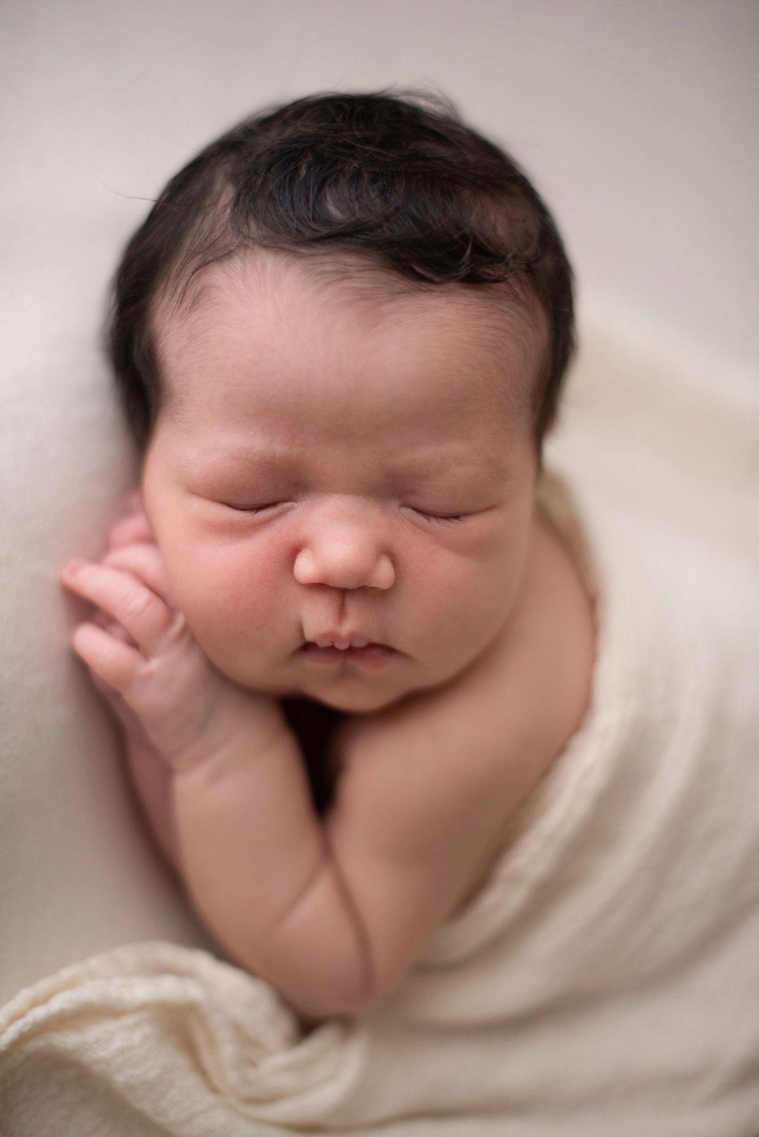Close-up of sleeping newborn wrapped in white fabric during professional photo session.