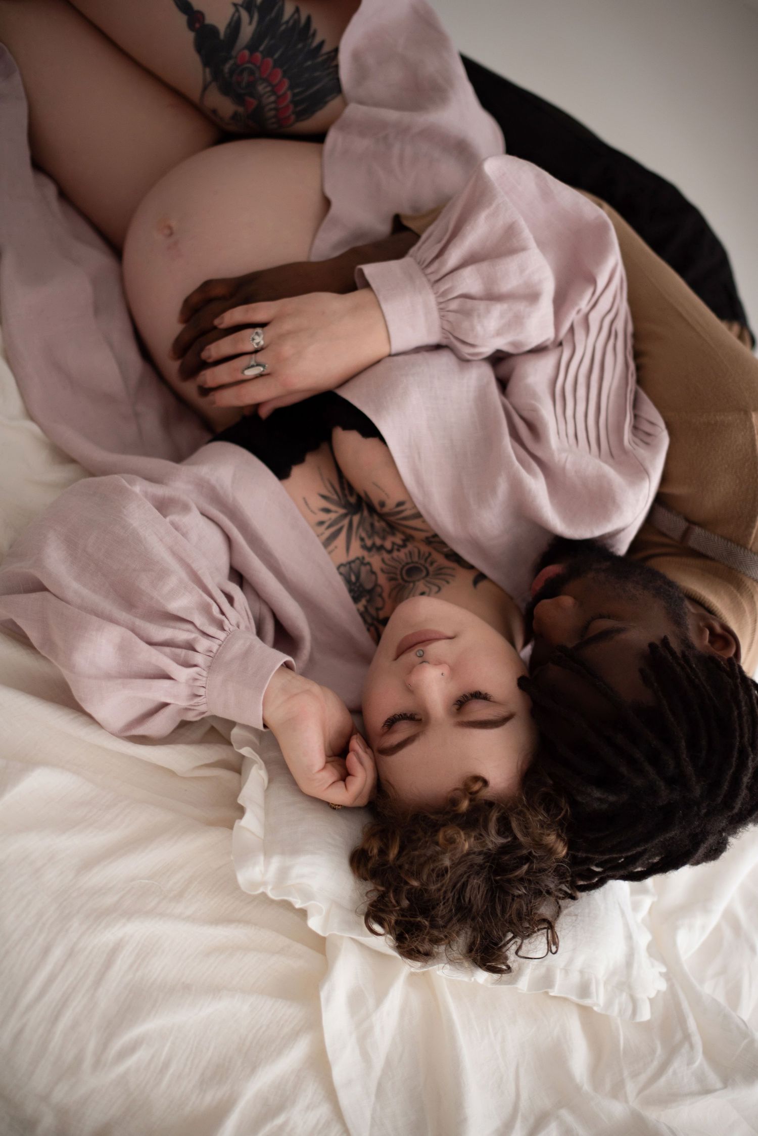 Artistic overhead maternity photo of couple lying on white bedding in intimate pose.