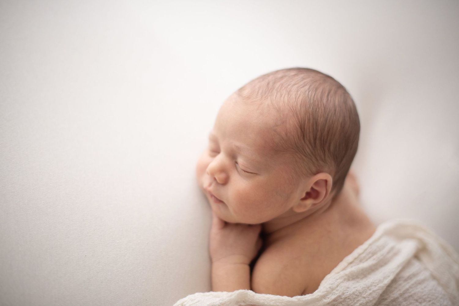 Peaceful sleeping newborn baby with hand under cheek on light background.