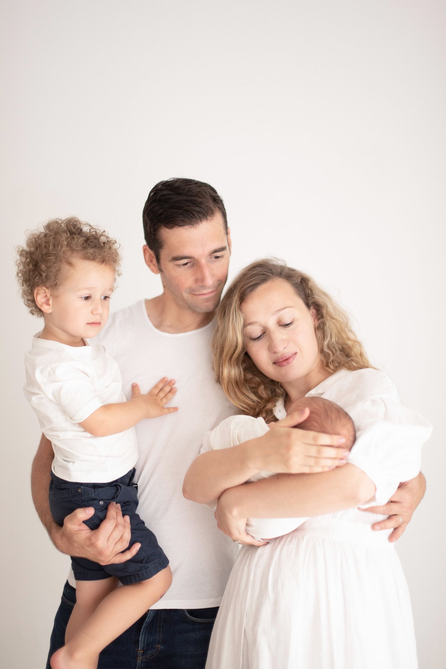 Family portrait with newborn baby in white against neutral background.