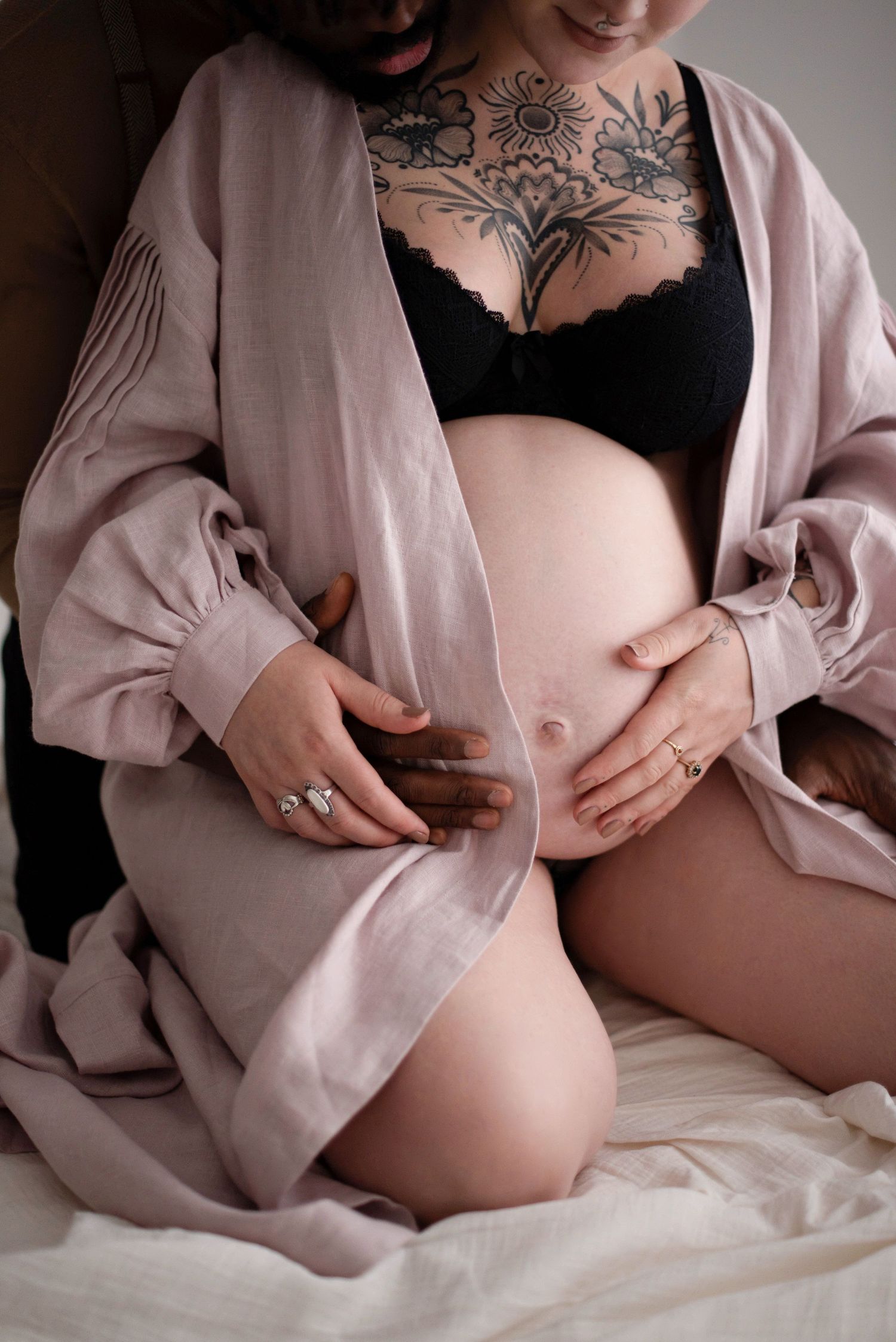 Detailed shot of pregnant belly with tattooed chest and pink robe against white background.