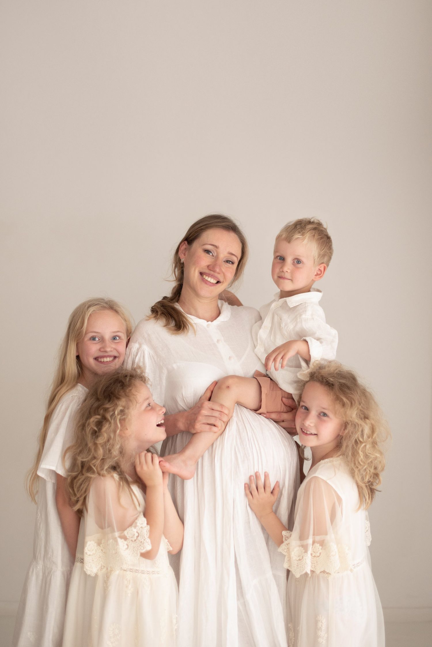 Family portrait with mother in white dress surrounded by children touching her pregnant belly.