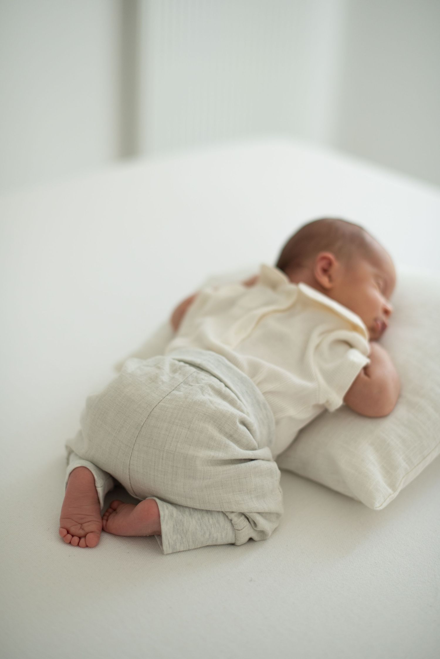 Baby sleeping on white surface wearing light colored linen outfit.